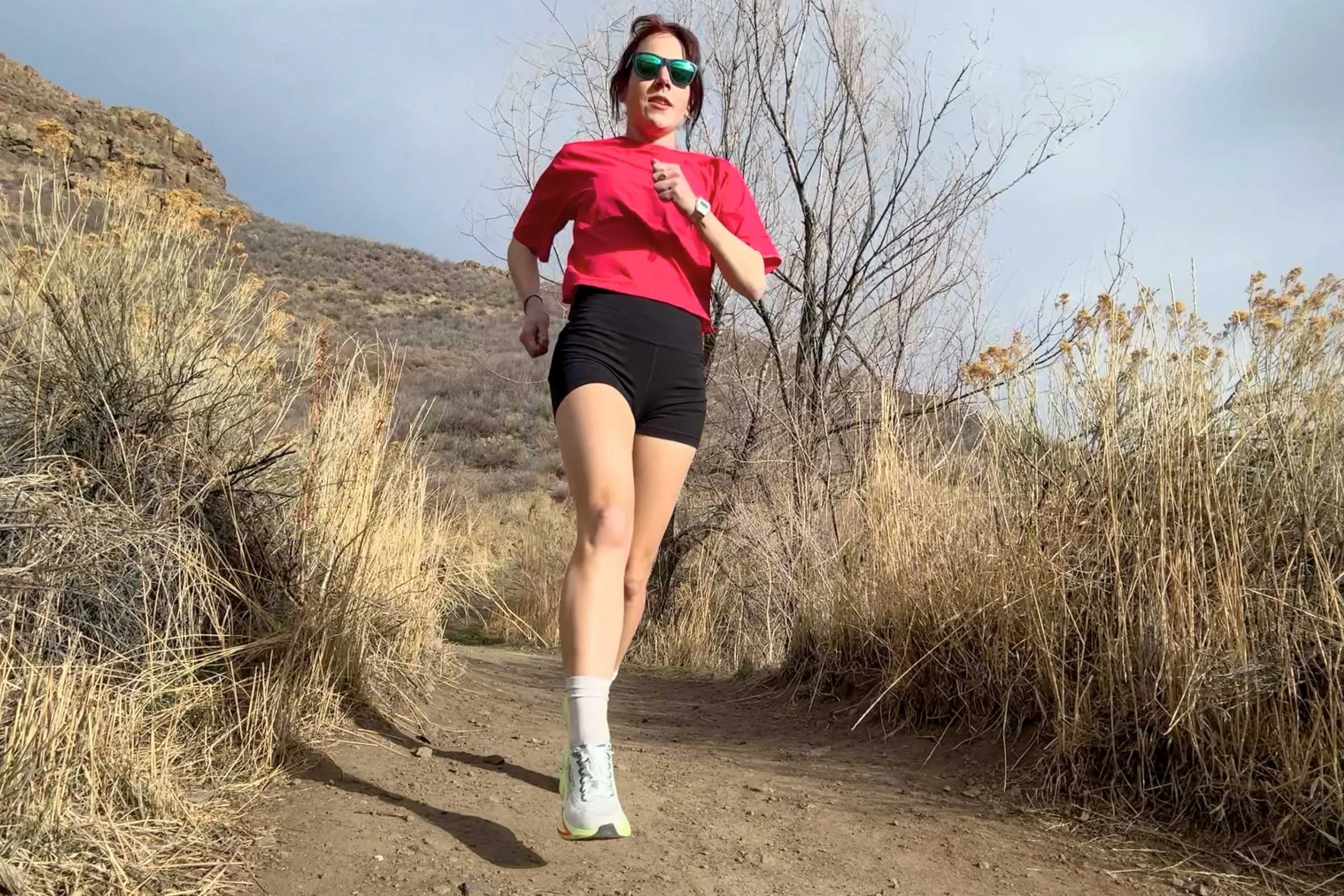   Woman running on a dirt trail wearing REI Co-op Swiftland Grid Running Shirt.  
