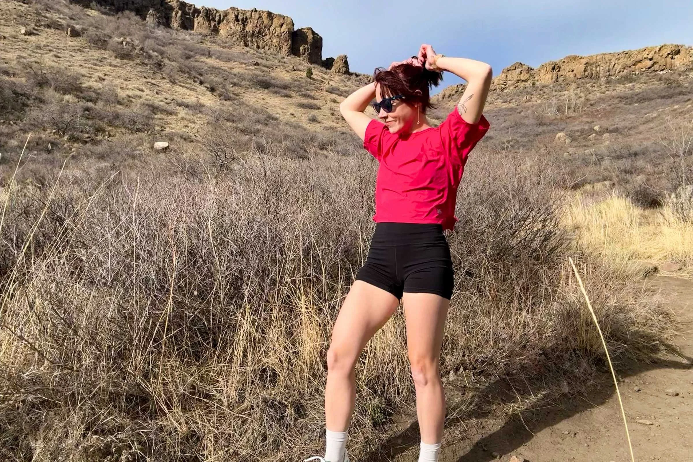   Woman cooling down after a trail run wearing REI Co-op Swiftland Grid Running Shirt in a dry, rocky landscape.  