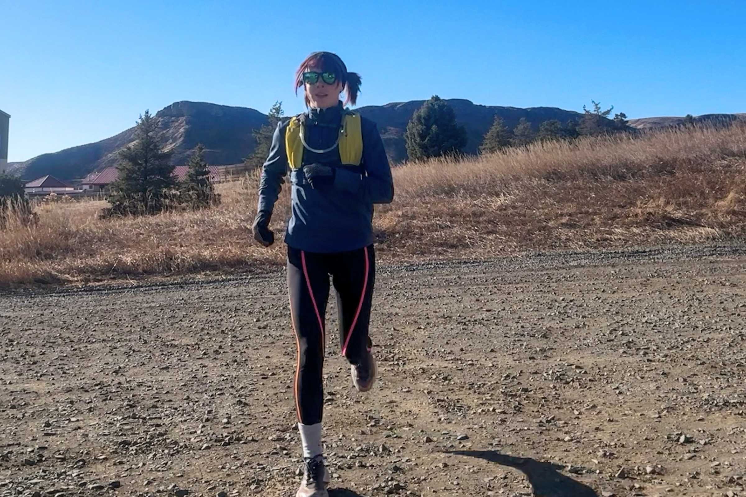   Runner running on a dirt trail wearing the REI Co-op Swiftland 5 Hydration Vest.  