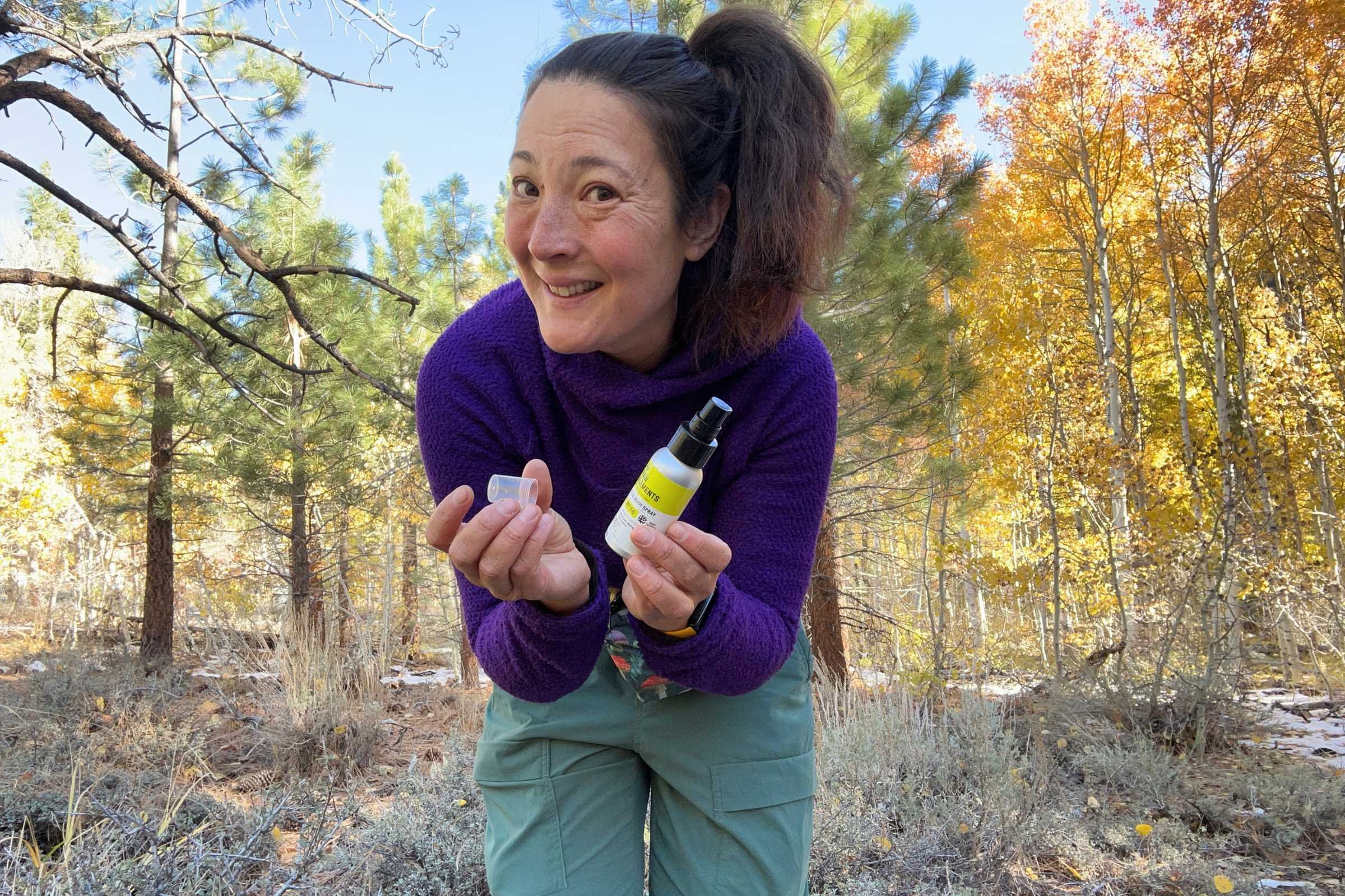   Gear tester holding Raw Elements SPF 50 mineral sunscreen spray while testing outdoors in autumn woods  