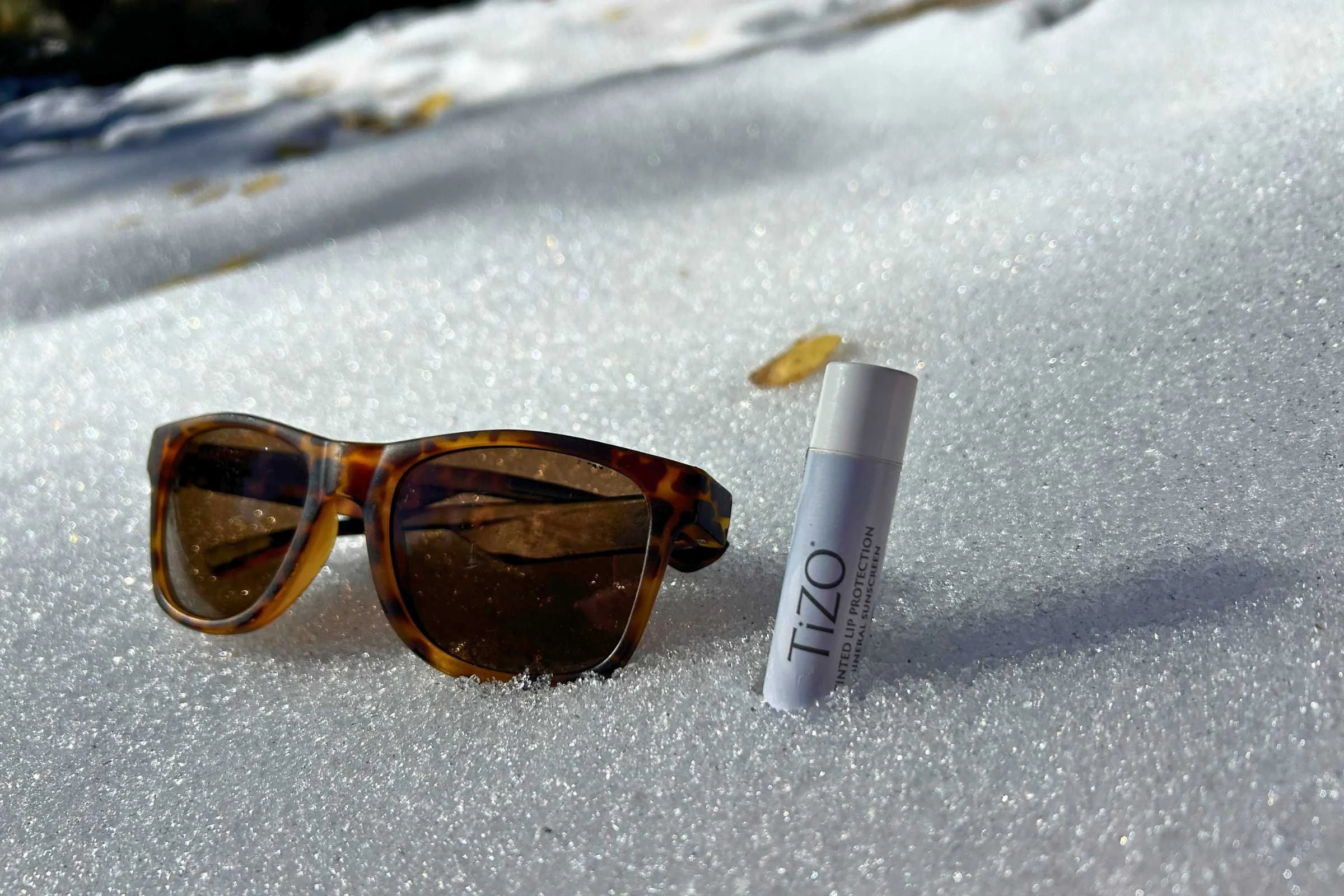   Tizo Lip Protection SPF 45 lip balm and sunglasses placed in snow during outdoor sun protection testing  