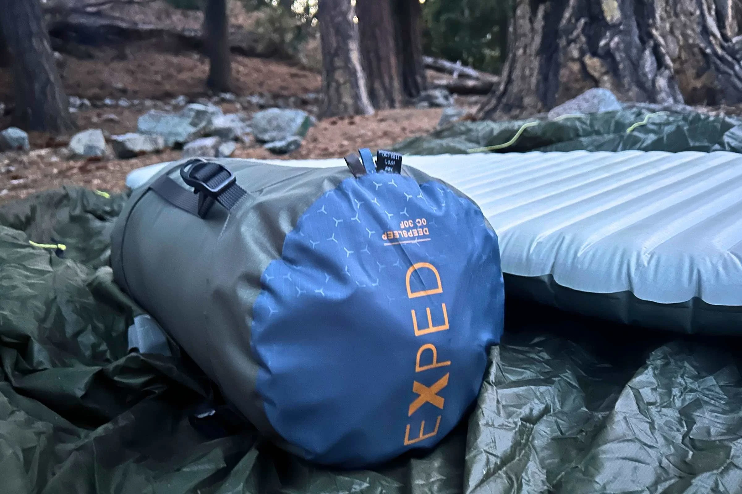   Exped DeepSleep sleeping bag packed into stuff sack beside sleeping pad at campsite  