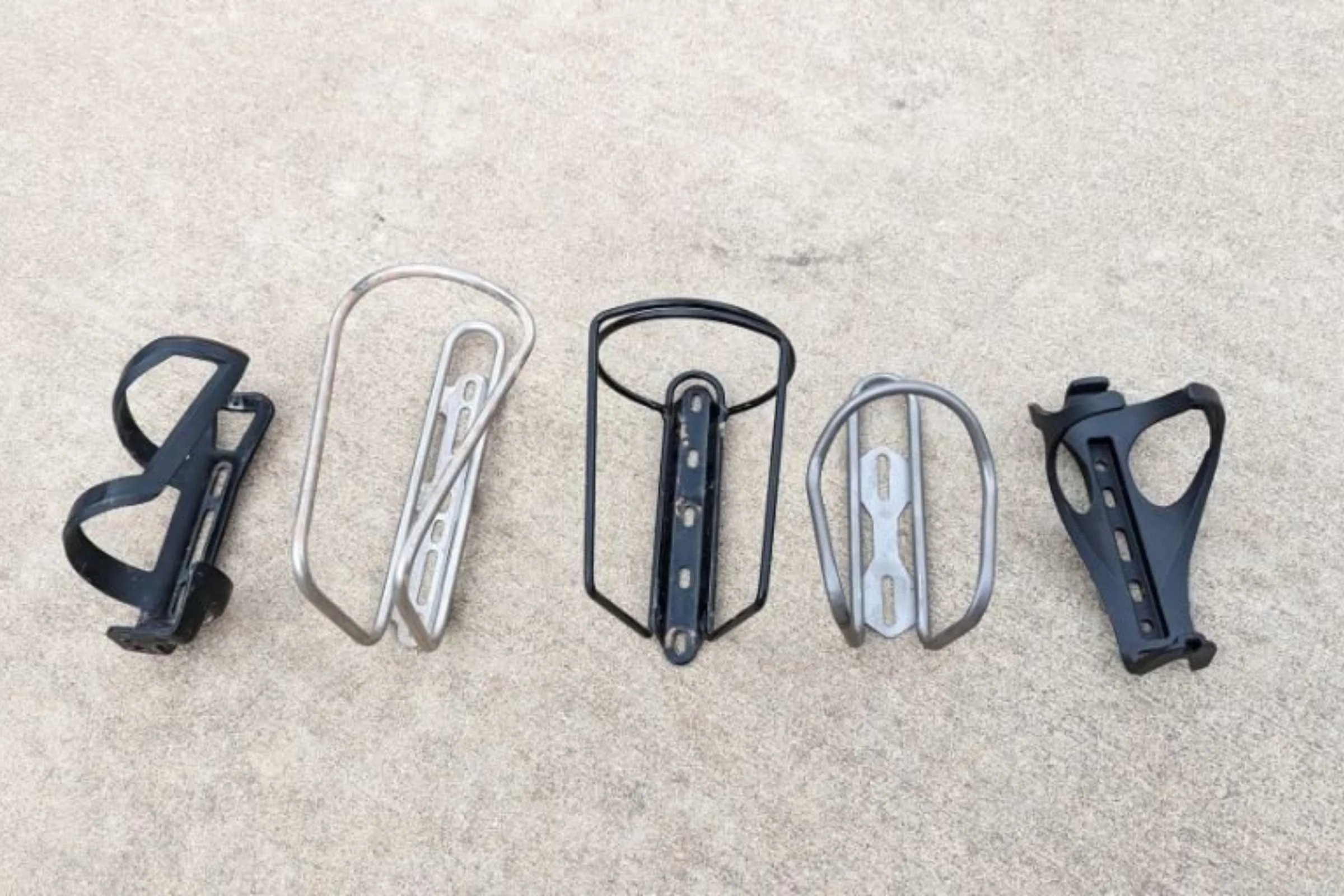   Some of the bike water bottle cages we considered. Left to right: Trek Side Load Recycled, Widefoot Litercage, Velo Orange Mojave, Silca Sicuro, Bontrager Bat Cage.  