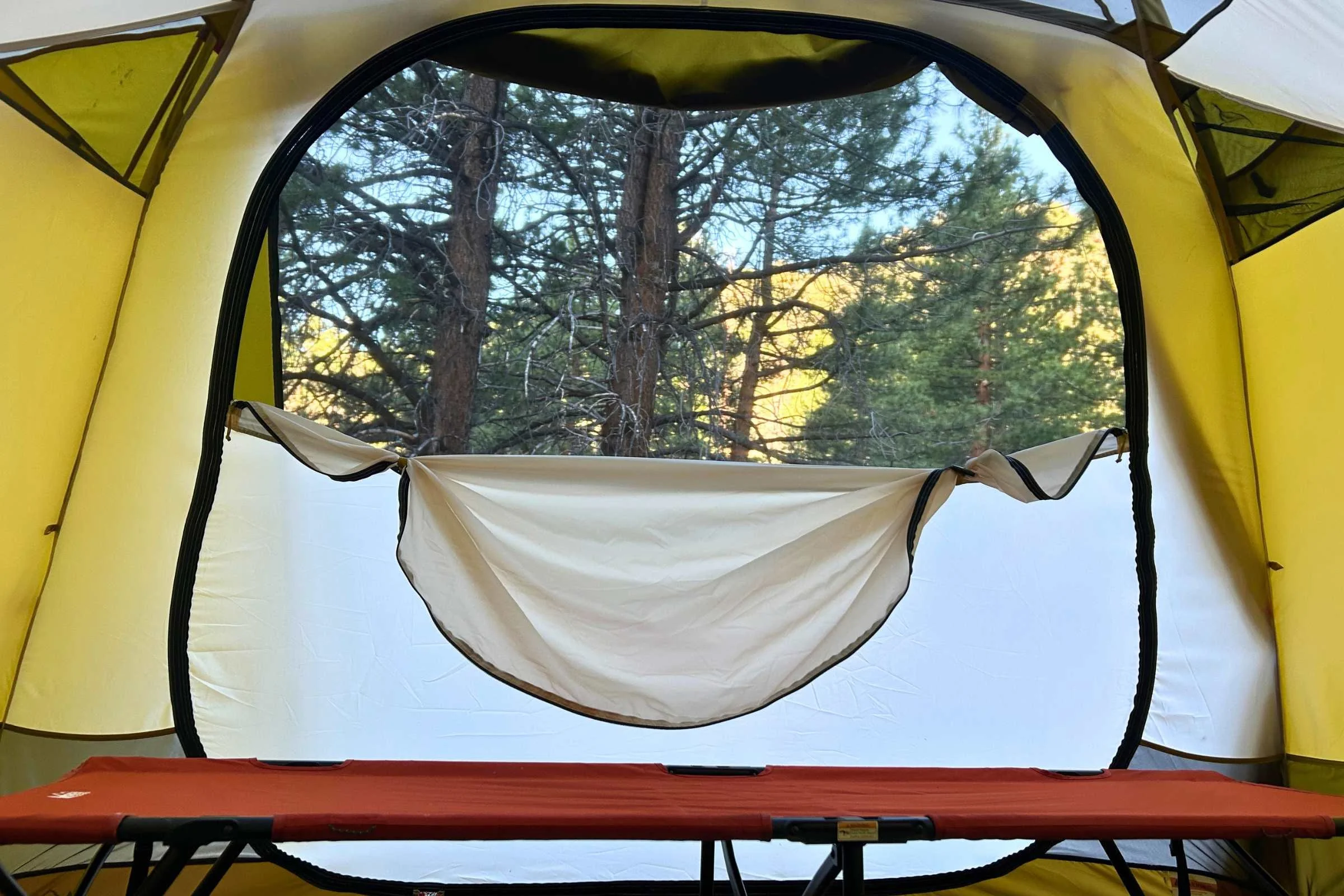   View from inside REI Base Camp 6 tent looking out the open door, with camping cot visible inside the tent  