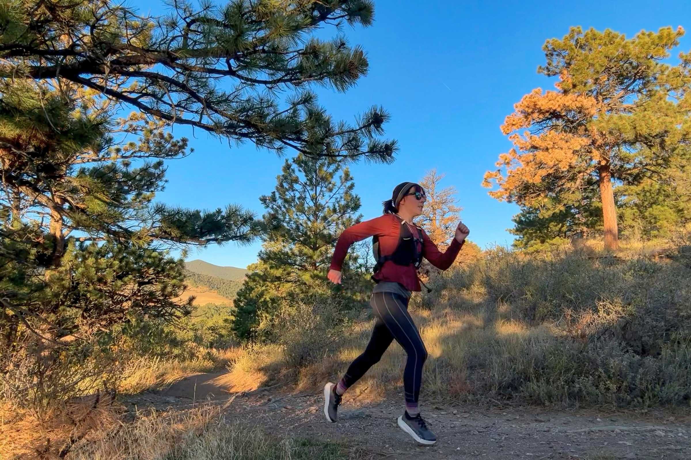   Side view of runner wearing Nathan HyperNight QuickStart 3.0 hydration pack on trail at sunrise  