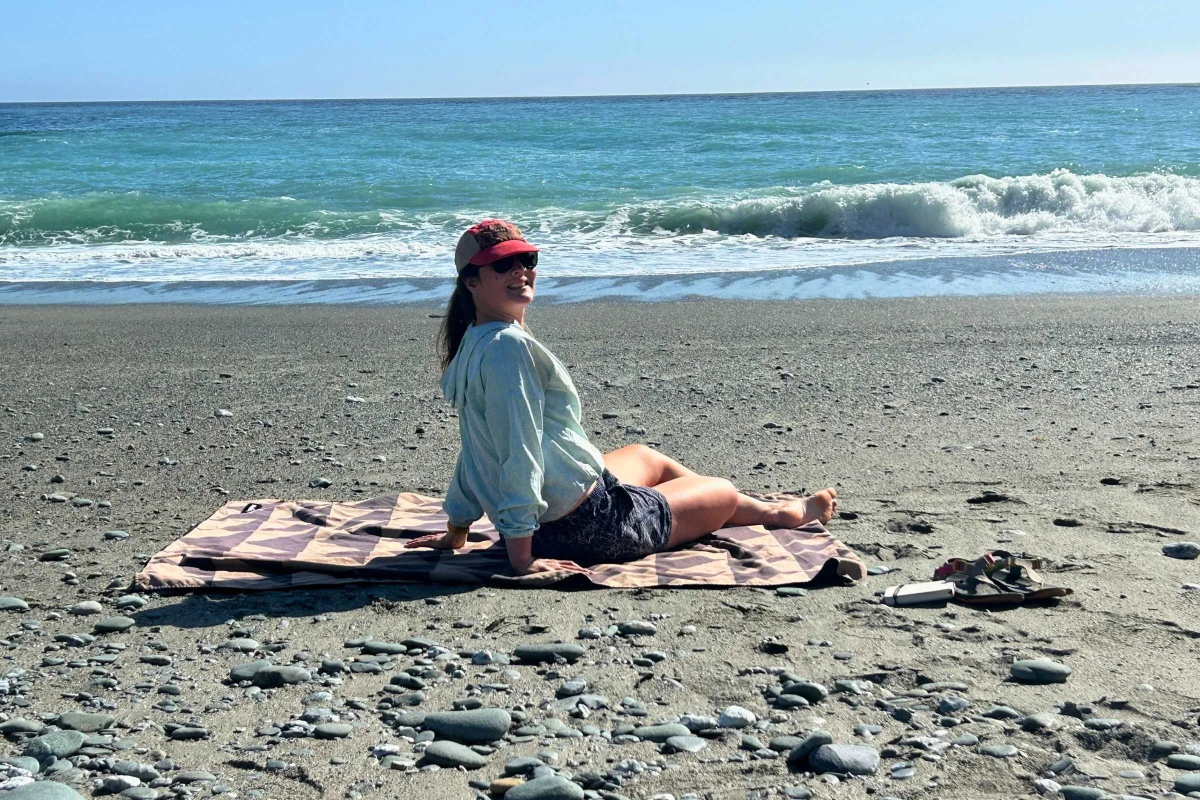   Woman wearing Royal Robbins Salathe Sun Shirt sitting on a beach blanket by the ocean  