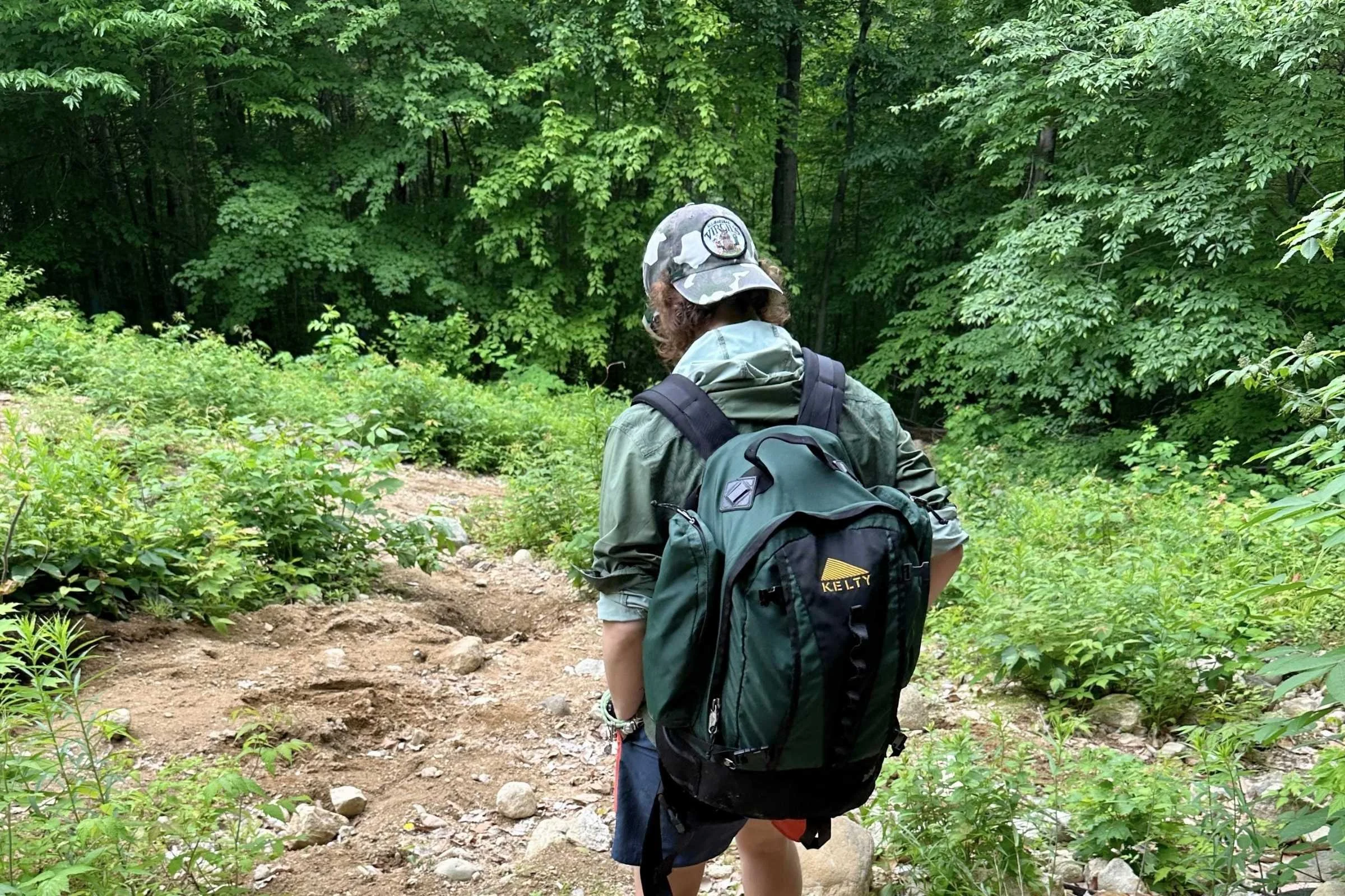   Rear view of hiker wearing Jolly Gear Triple Crown Button Down with backpack on wooded trail  