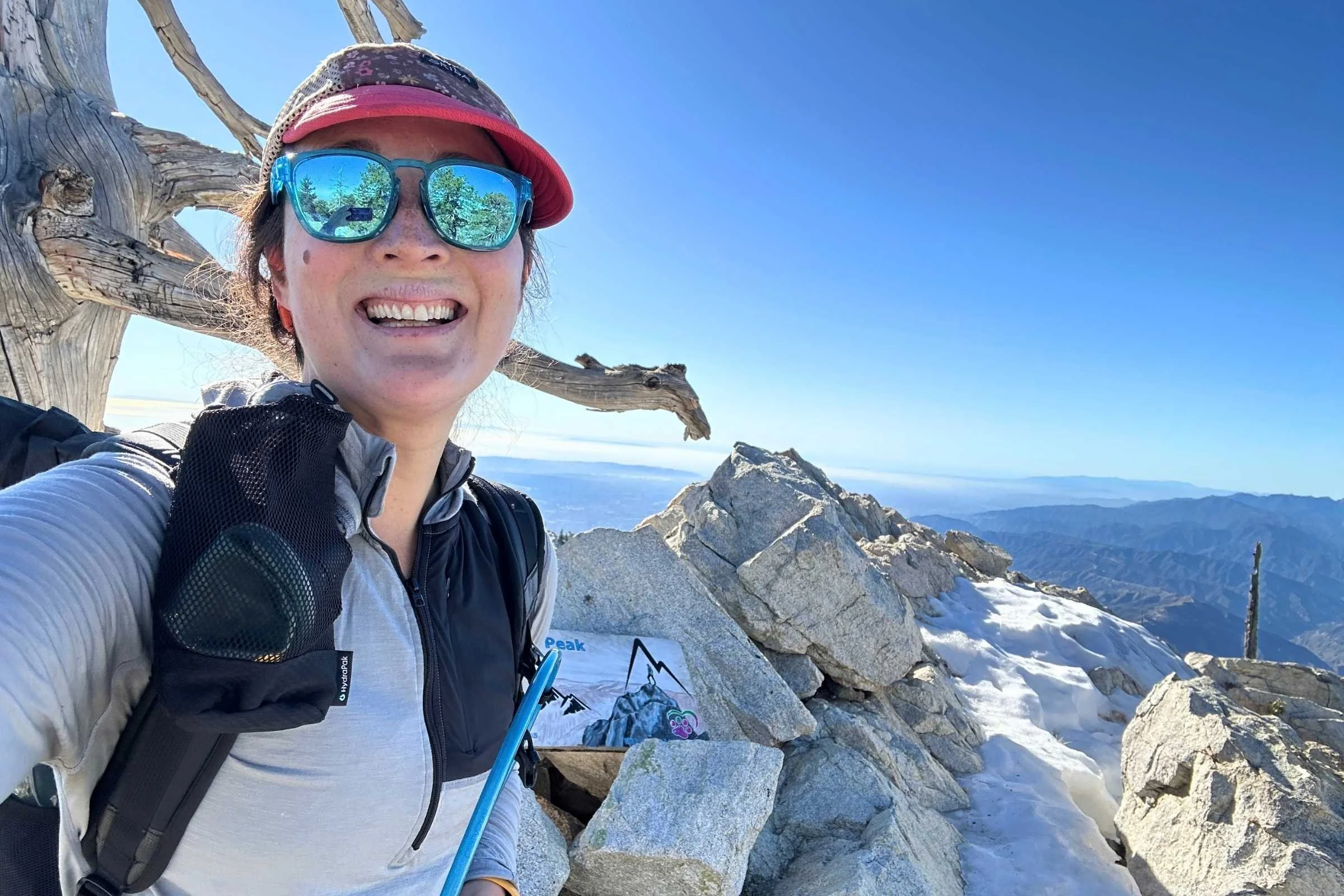   Woman wearing Ridge Merino Solstice Pro Hoodie with hydration vest on snowy mountain summit  