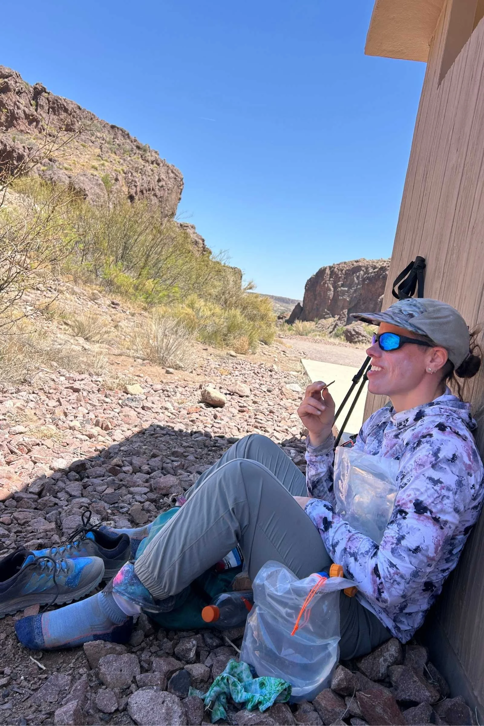   Woman wearing Outdoor Research Echo Hoodie while taking a break in the shade of a building in the desert with backpack and hiking gear  