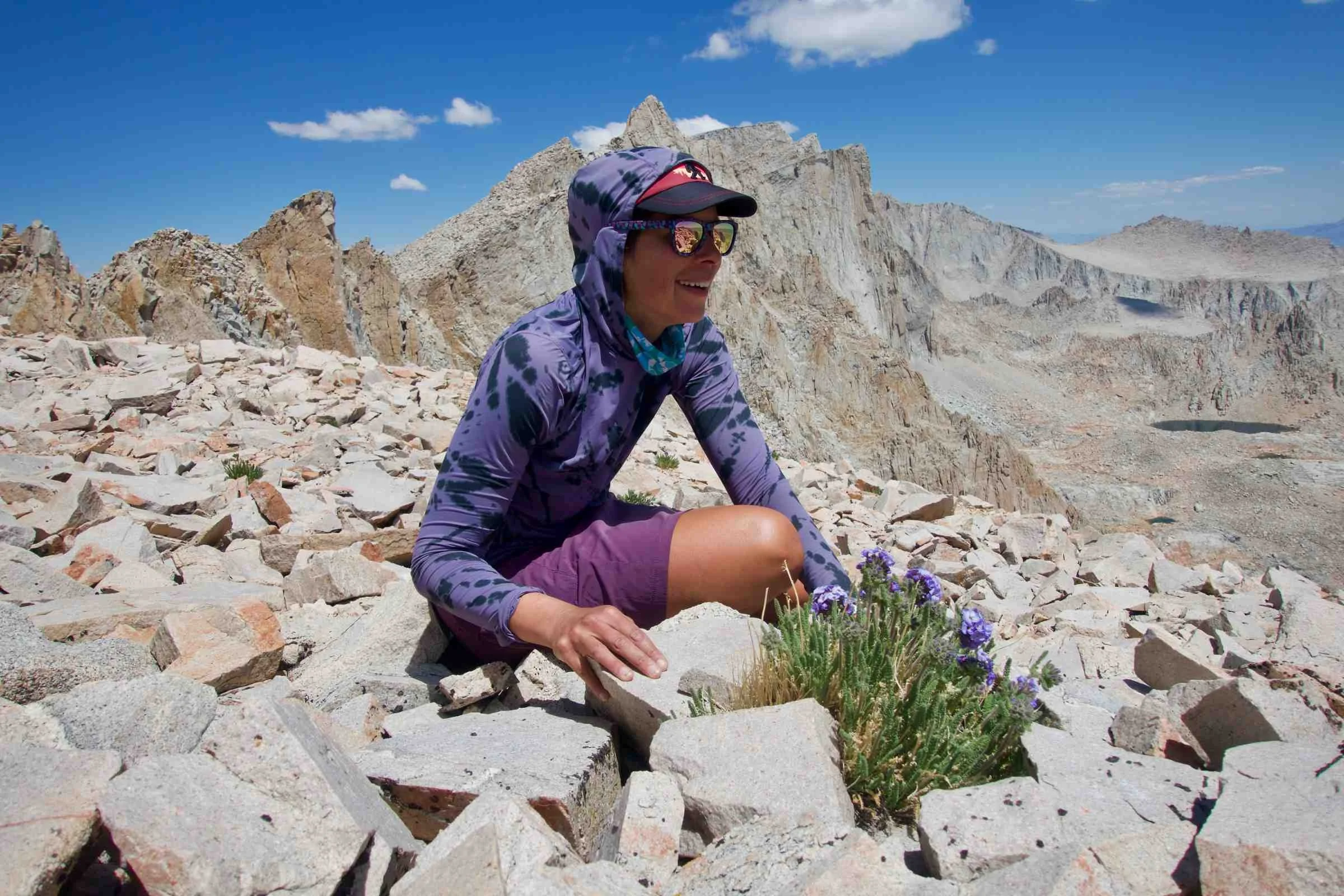   Woman wearing Mountain Hardwear Crater Lake Hoody crouched next to a patch of alpine wildflowers  