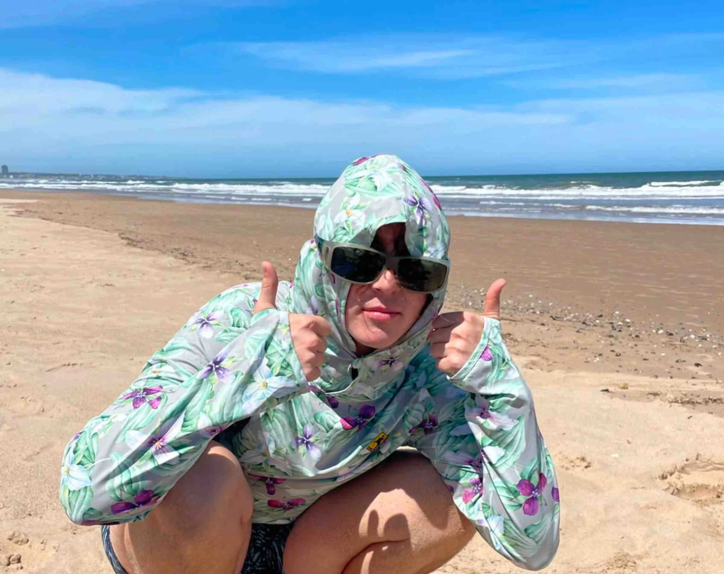   Person wearing Town Shirt Sun Hoodie with hood up and thumbs through thumbholes on the beach  