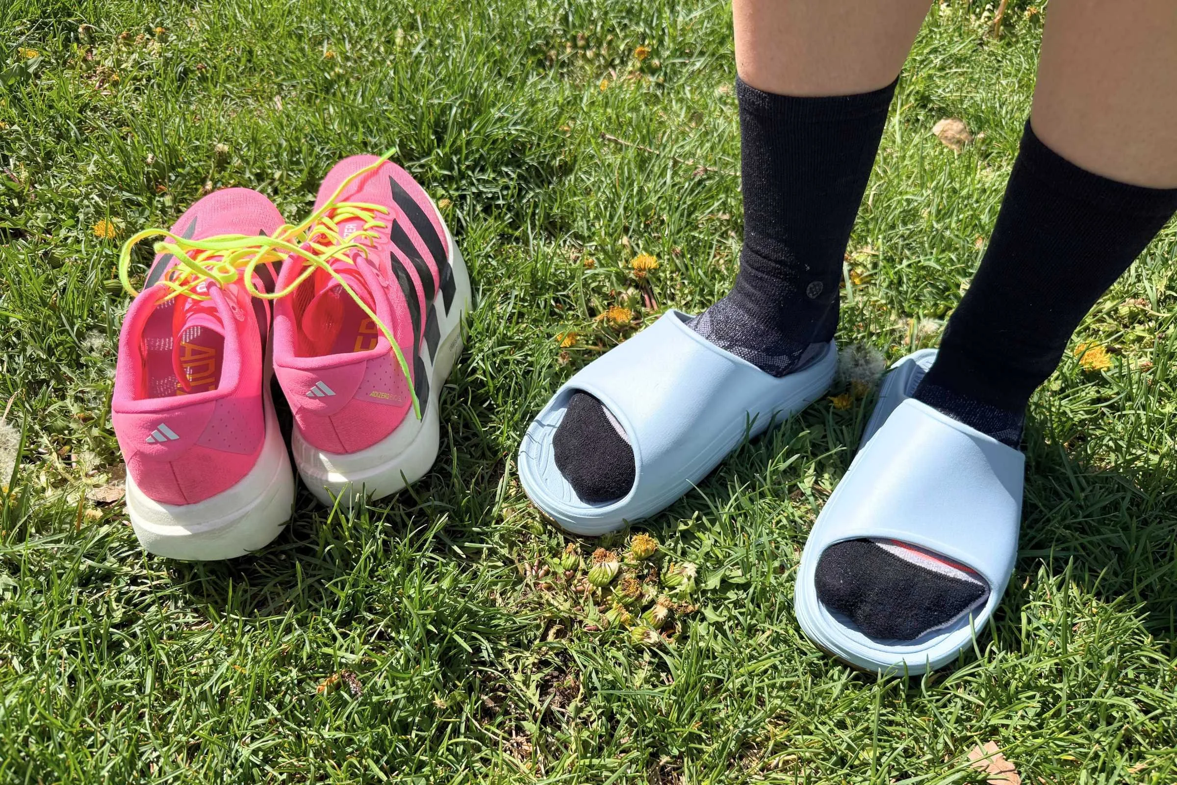   Person wearing norda 008 recovery slides next to running shoes on grass  