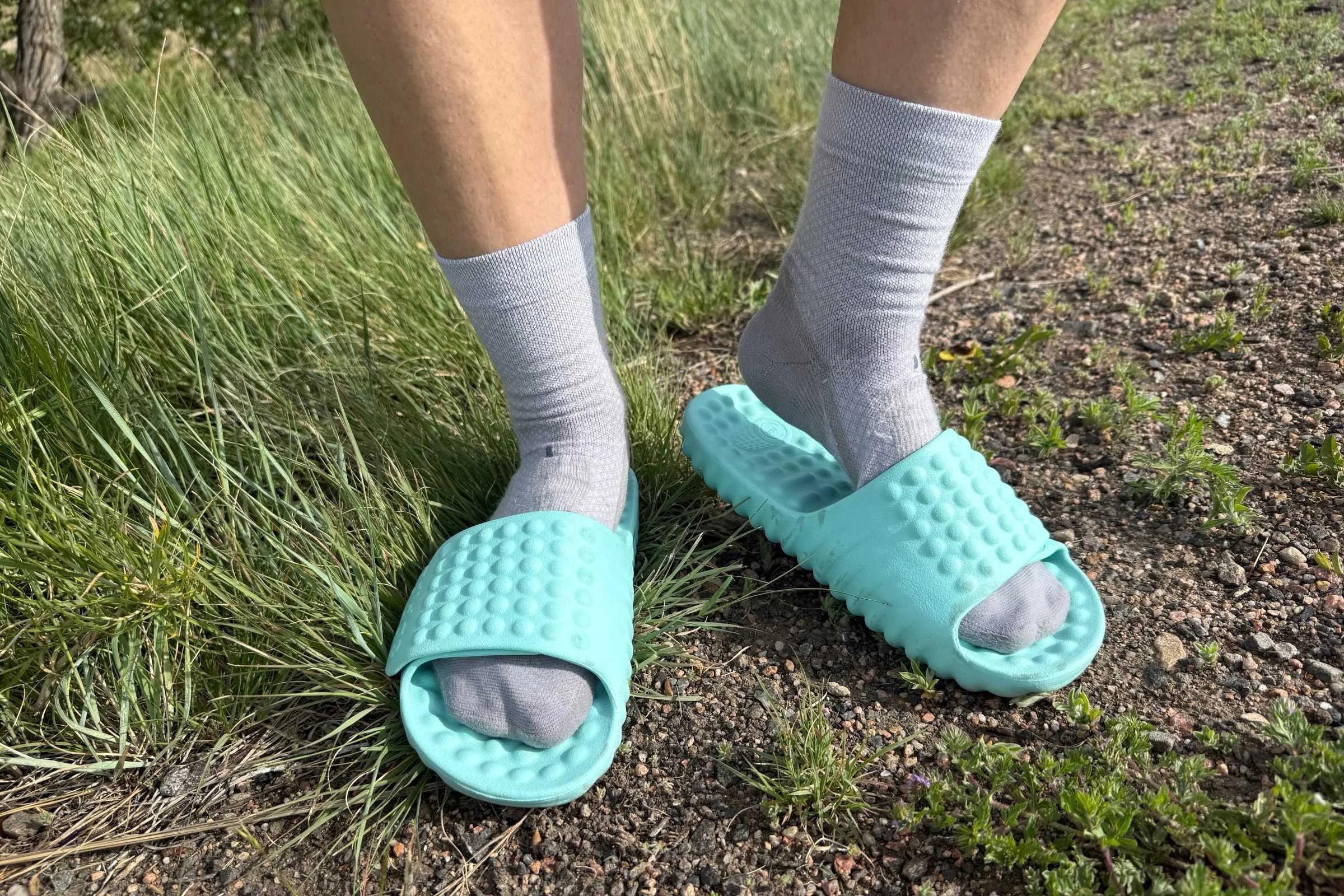   Person wearing Adidas Adissage 360rec Slides with socks on grassy trail  