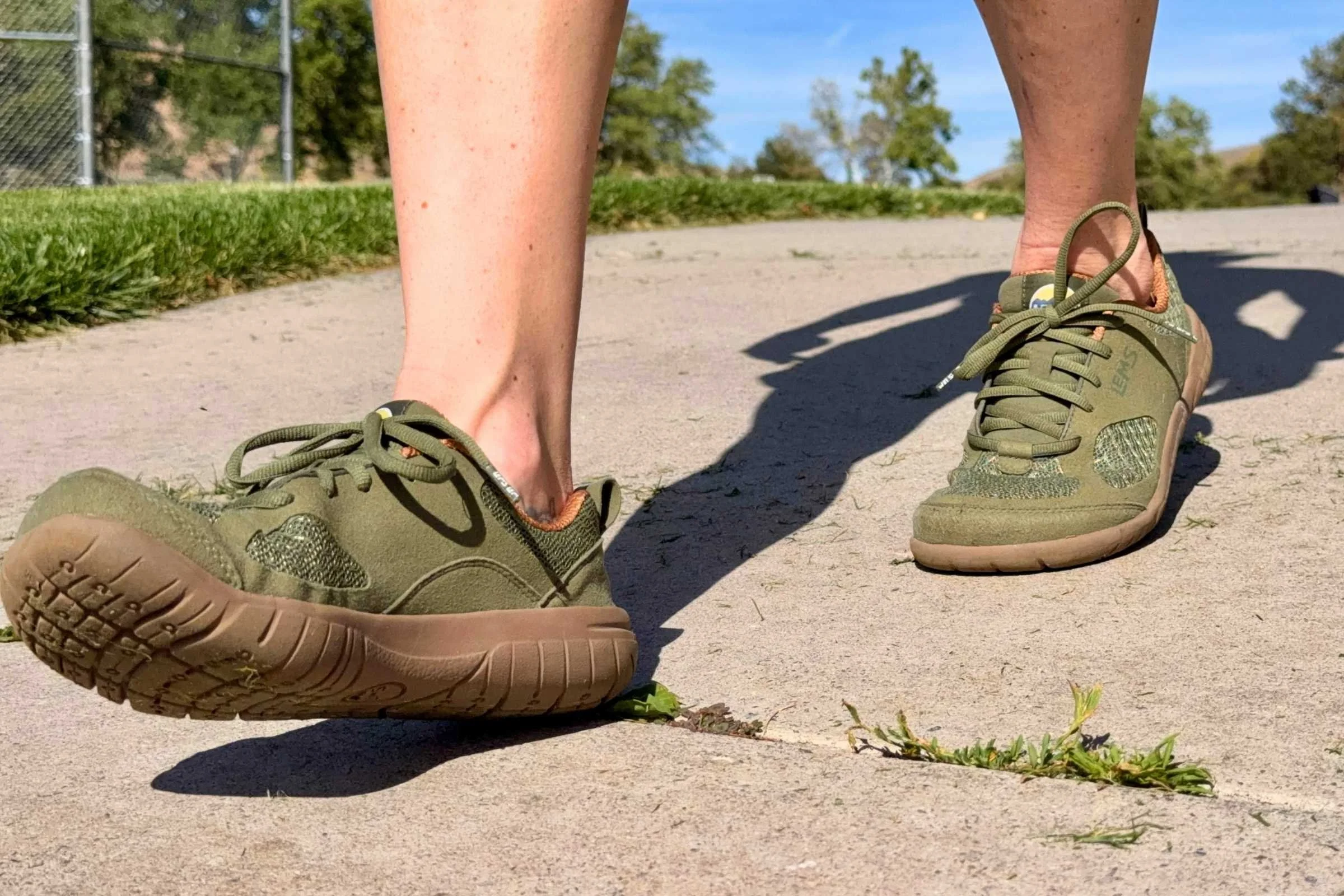   Close-up of the feet of a person wearing Lems Primal 3 barefoot shoes while walking on pavement  