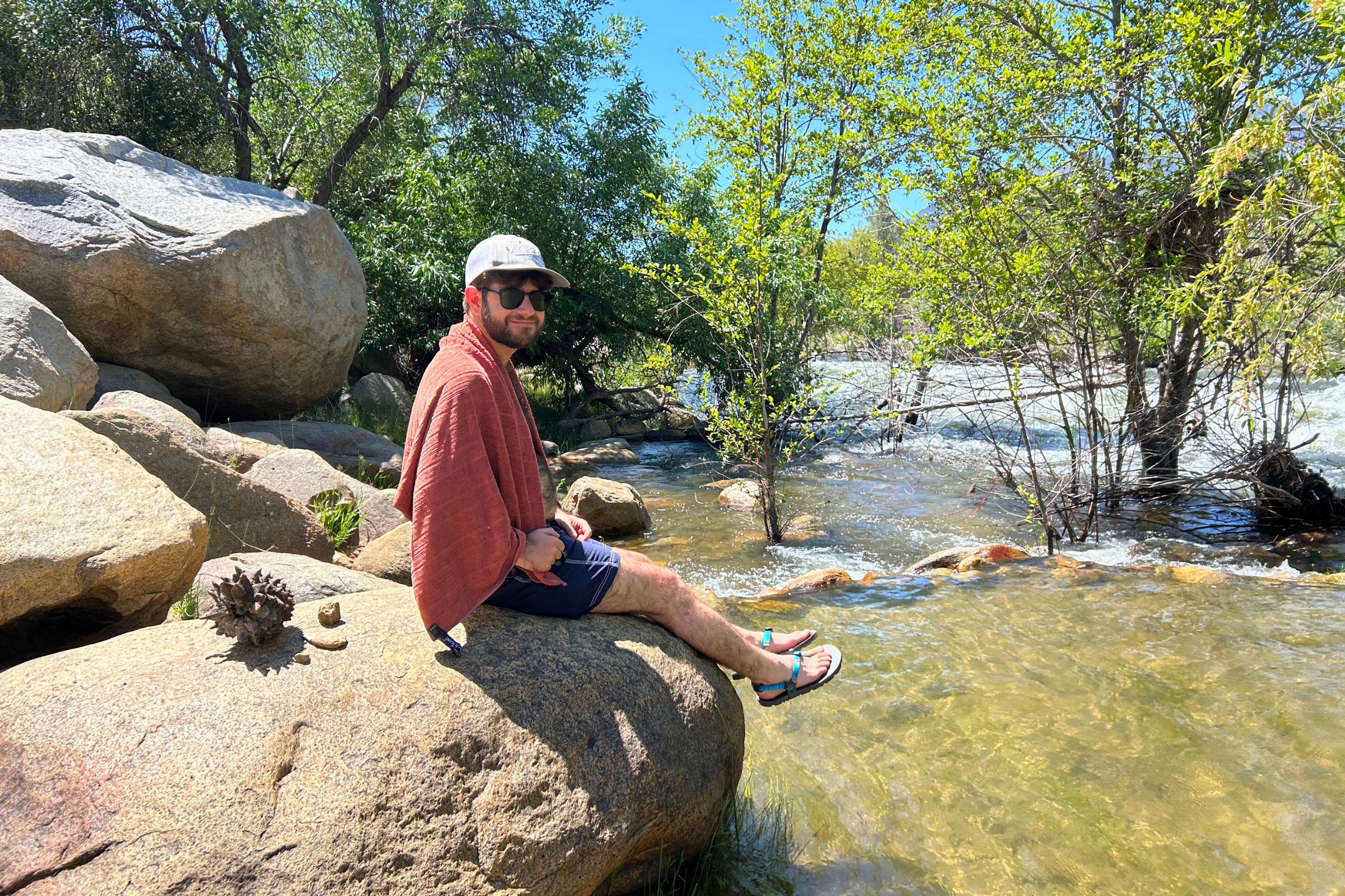   Man using the REI Multi-Towel Deluxe to dry off down by a river  