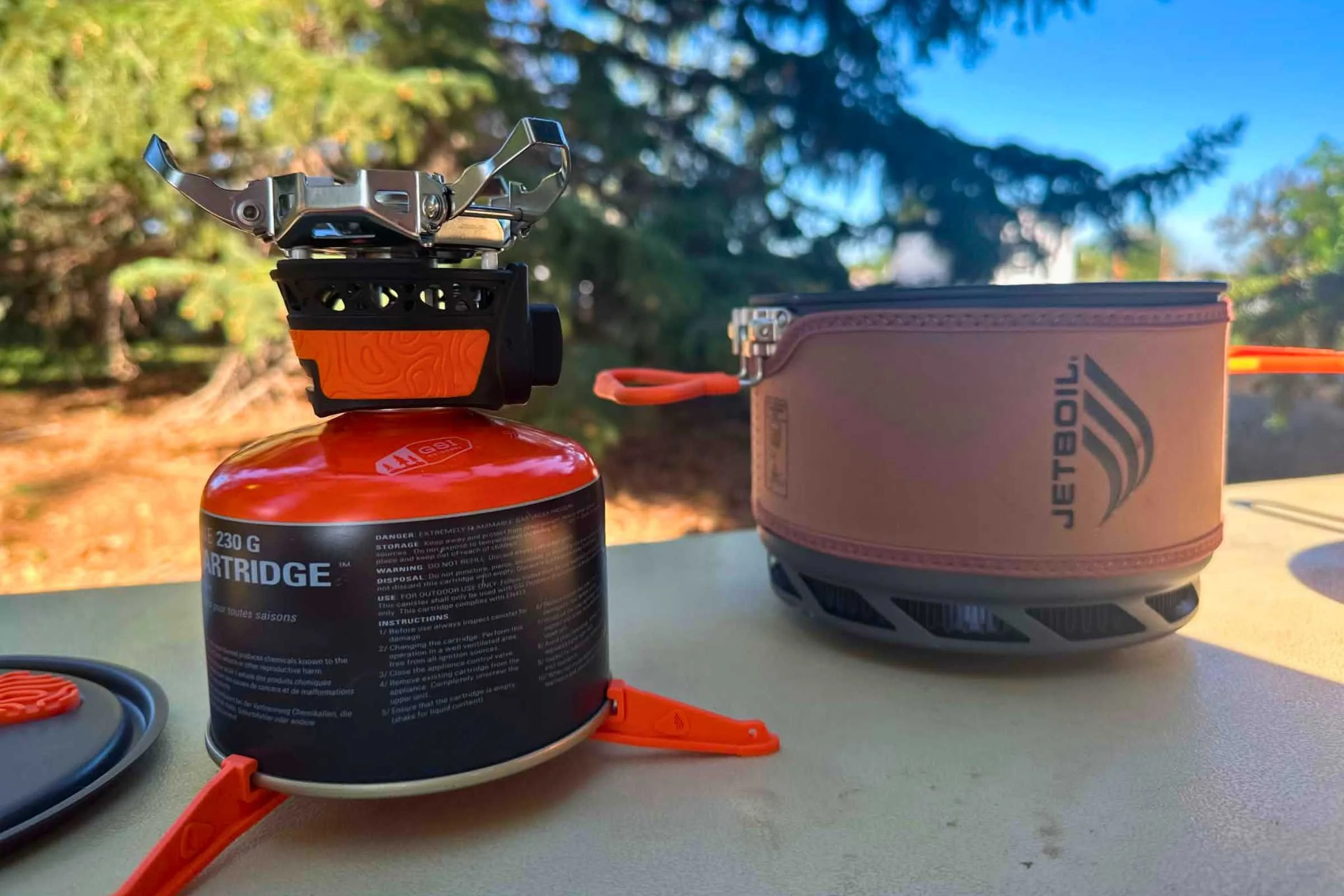   The burner attached to an isobutane/propane canister and plastic base with the pot and pot lid on either side.  