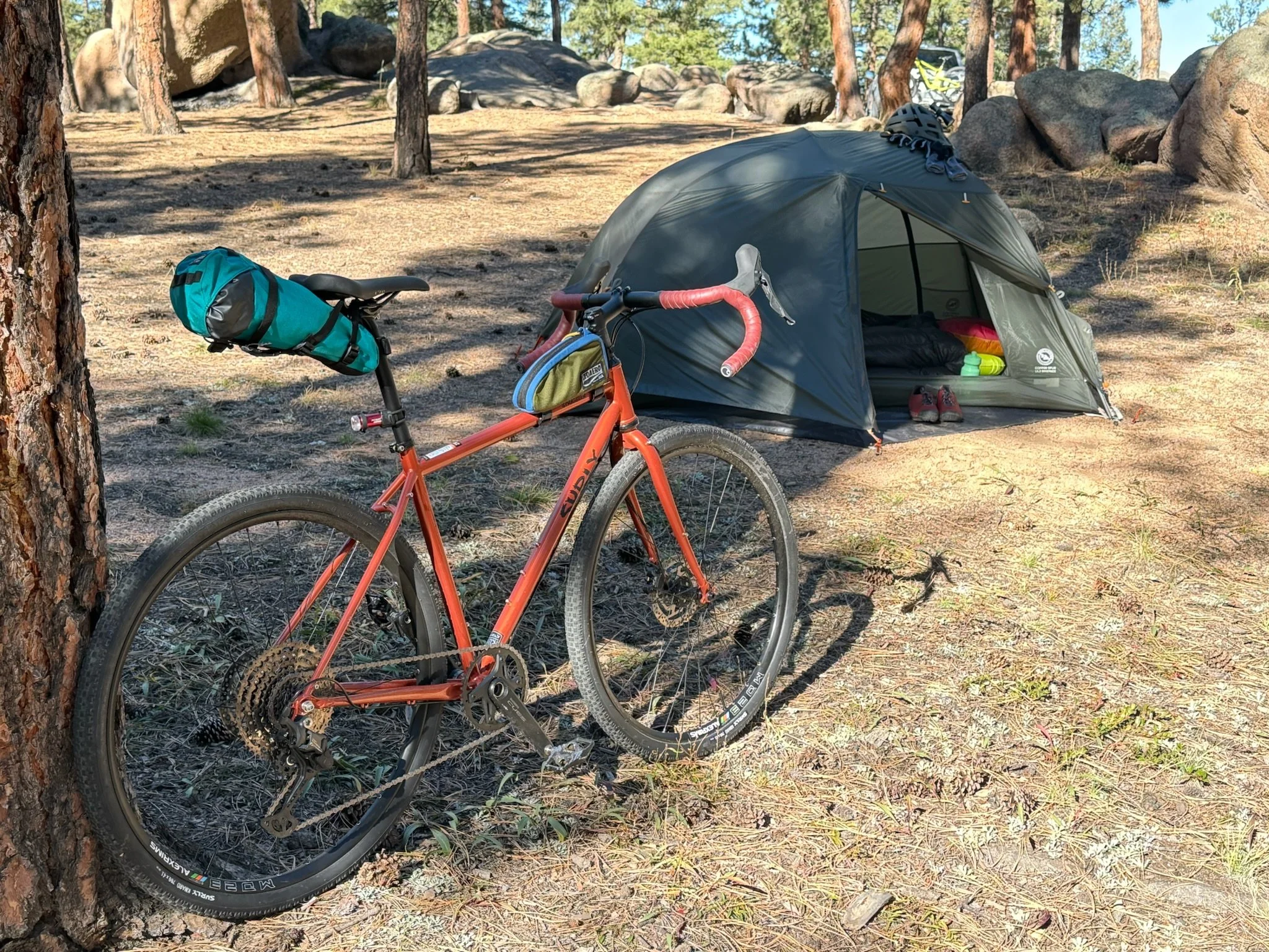   The loaded Straggler sits beside a tent at camp, showing how it can carry gear for overnight bikepacking trips.  