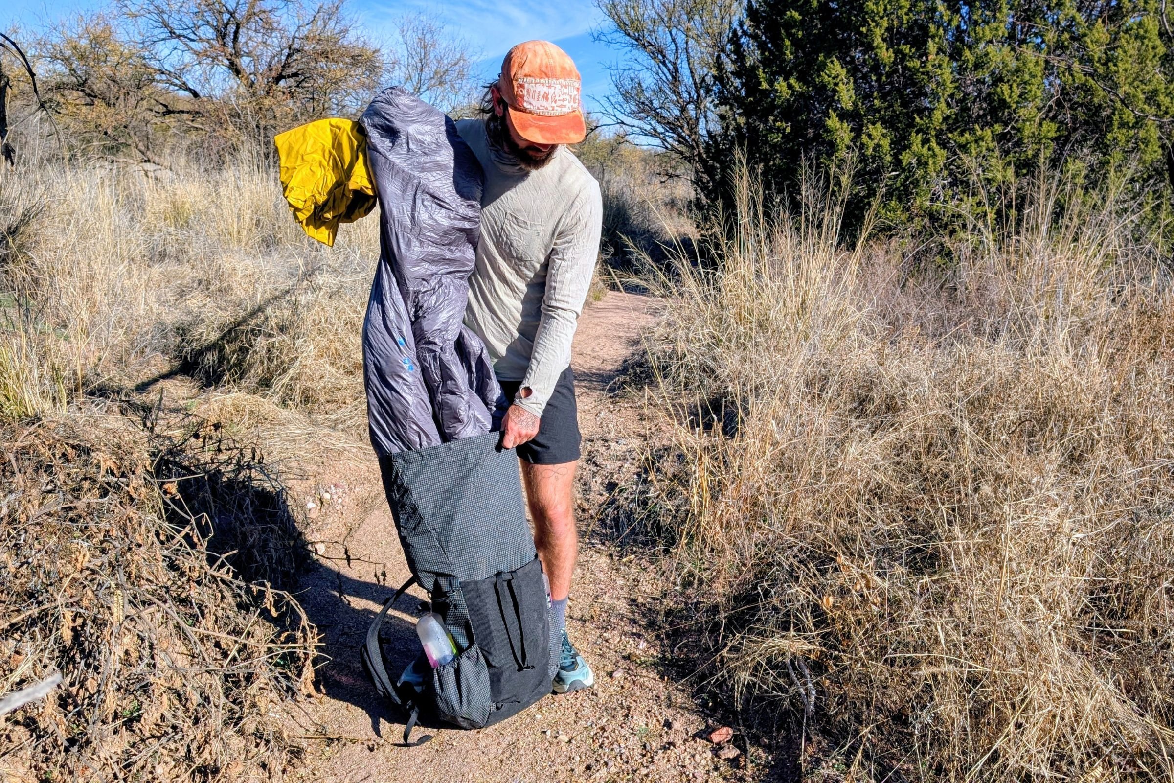   A hiker adjusts removing gear from the Pa’lante V2 with Joey Straps while standing on a dry desert trail.  