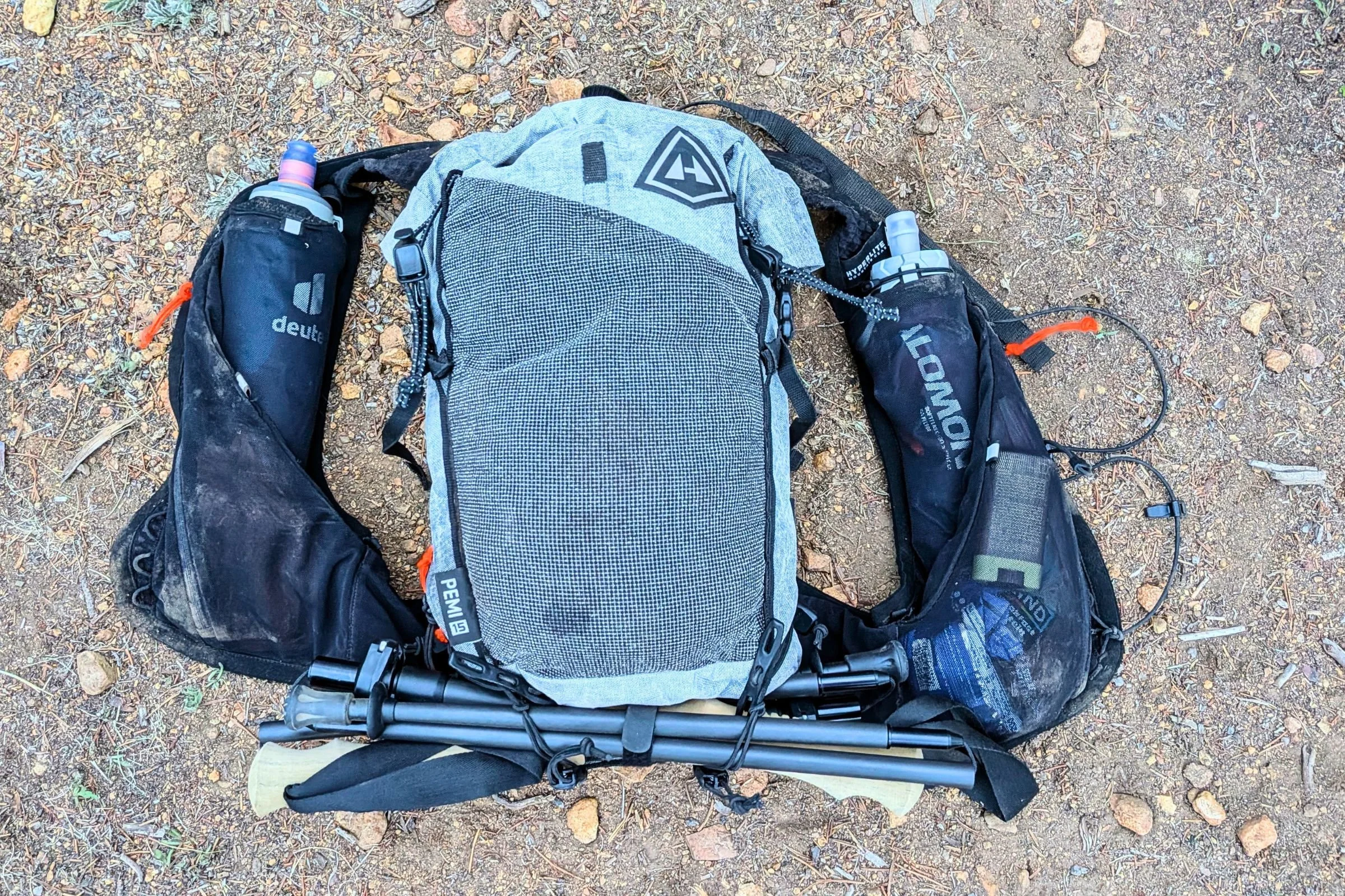   The Hyperlite Mountain Gear Pemi 15 is laid out with its shoulder-strap pockets, stretch-mesh storage, and trekking poles, showing how much gear can fit in this compact fastpack.  