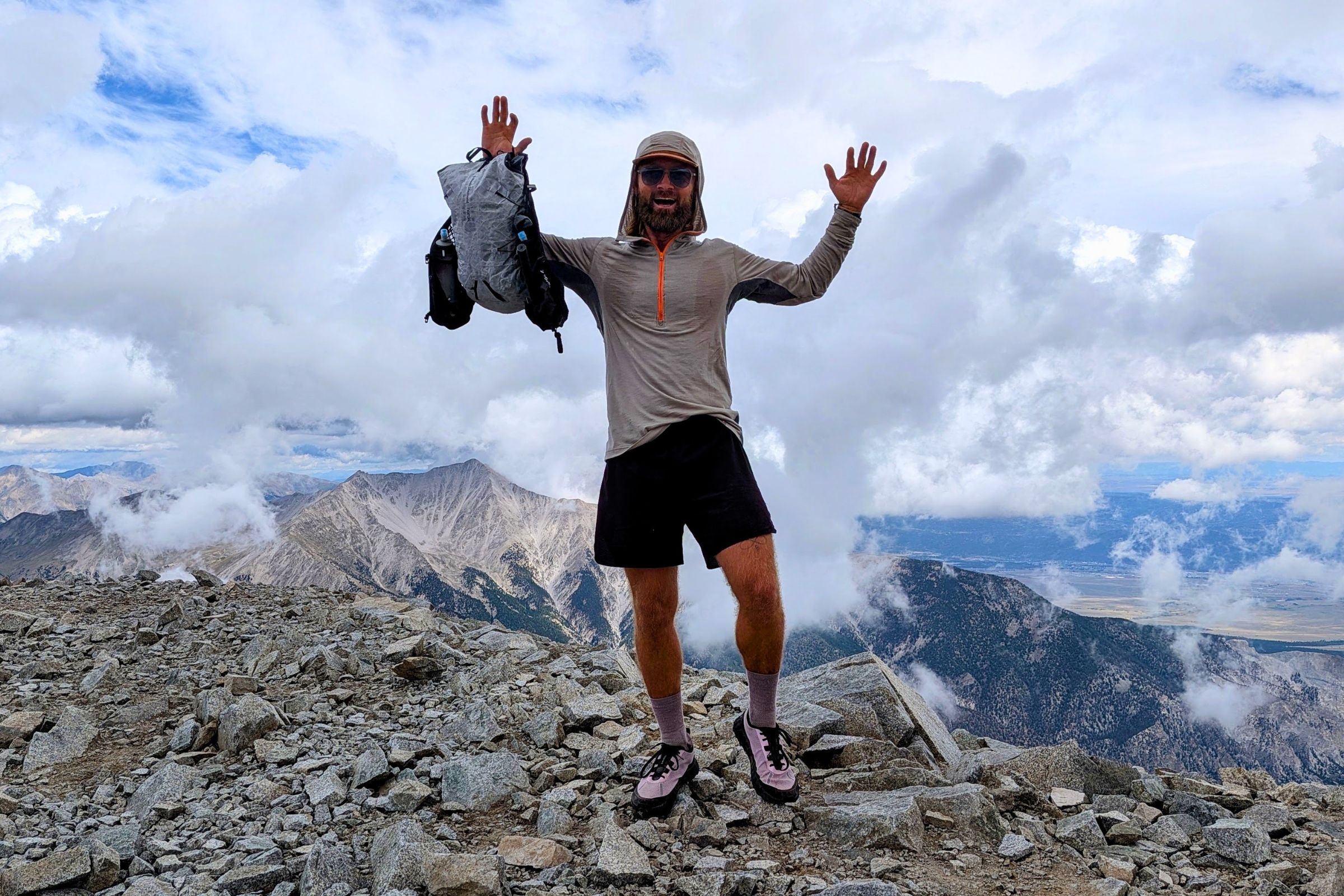   A tester holding the Black Diamond Distance 15 overhead after reaching a rocky mountain summit.  