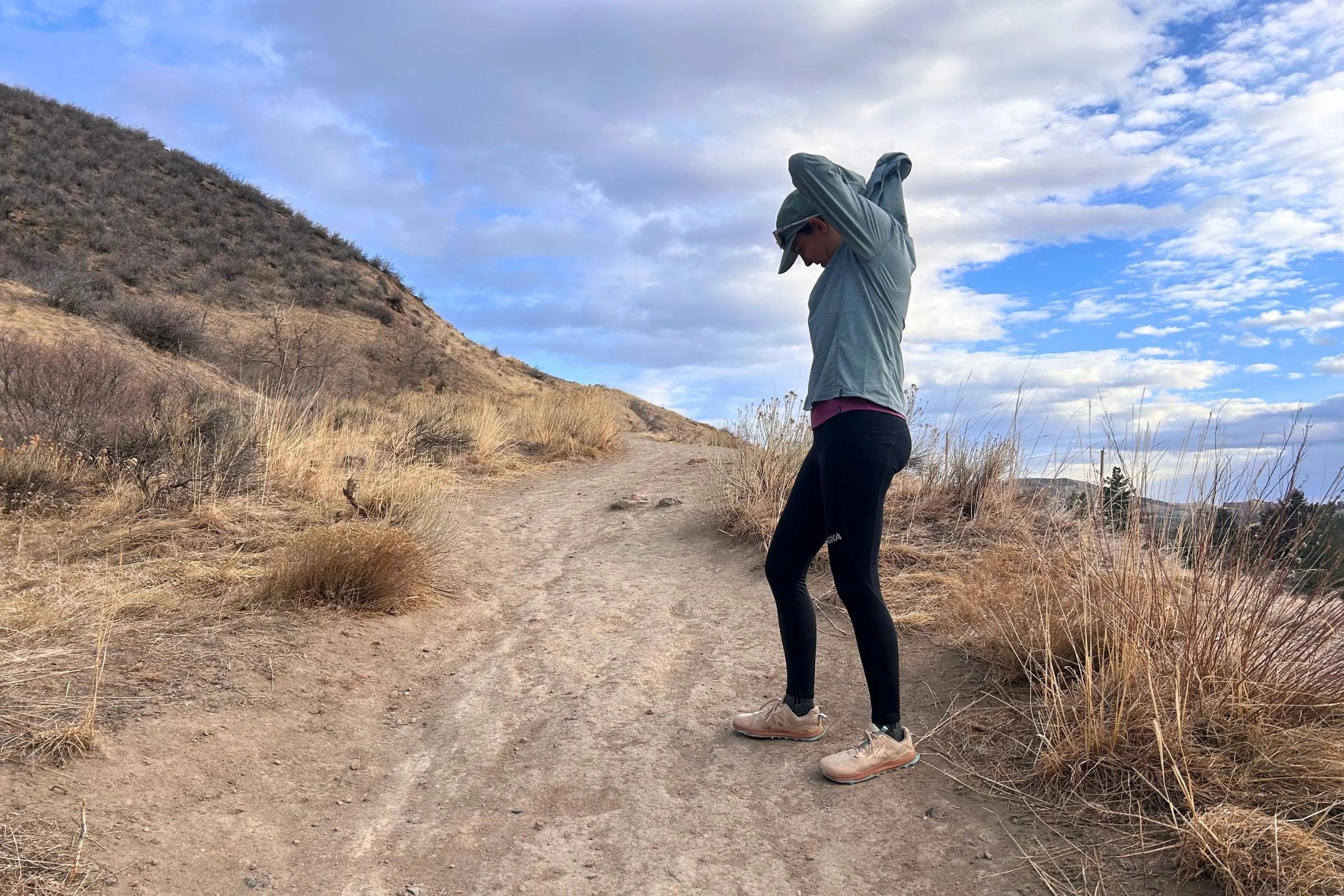   A runner adjusting the hood of the Patagonia Capilene Cool Sun Hoody while on a trail.  