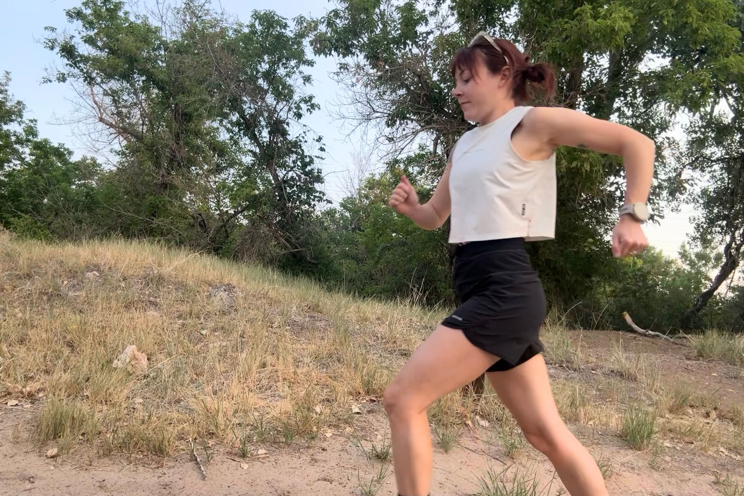   A runner wearing the ASRV x Equinox Aerosilver Cropped Training Tank on a sunny trail.  