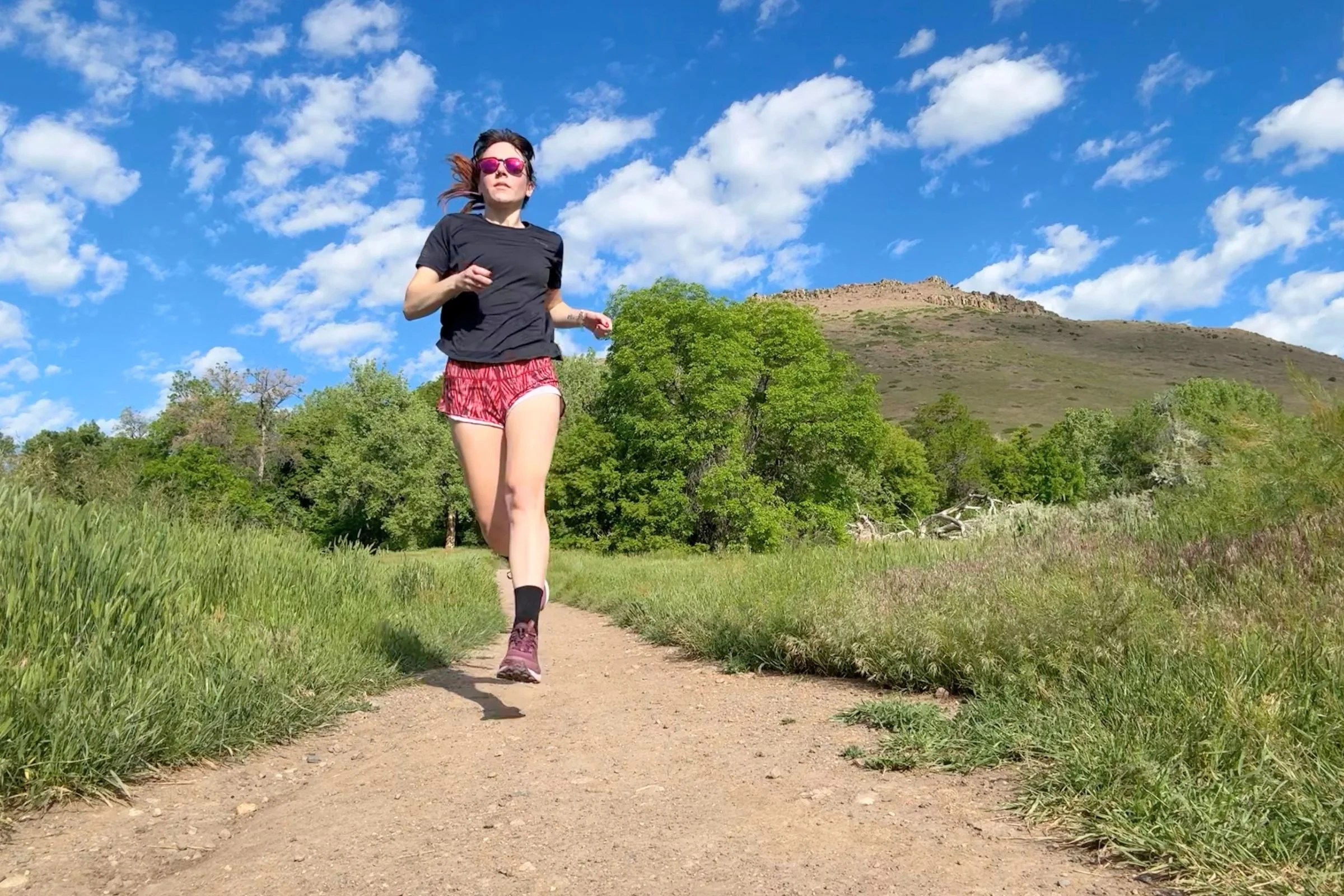   A runner wearing the Janji Run All Day Tee while running on a sunny trail.  