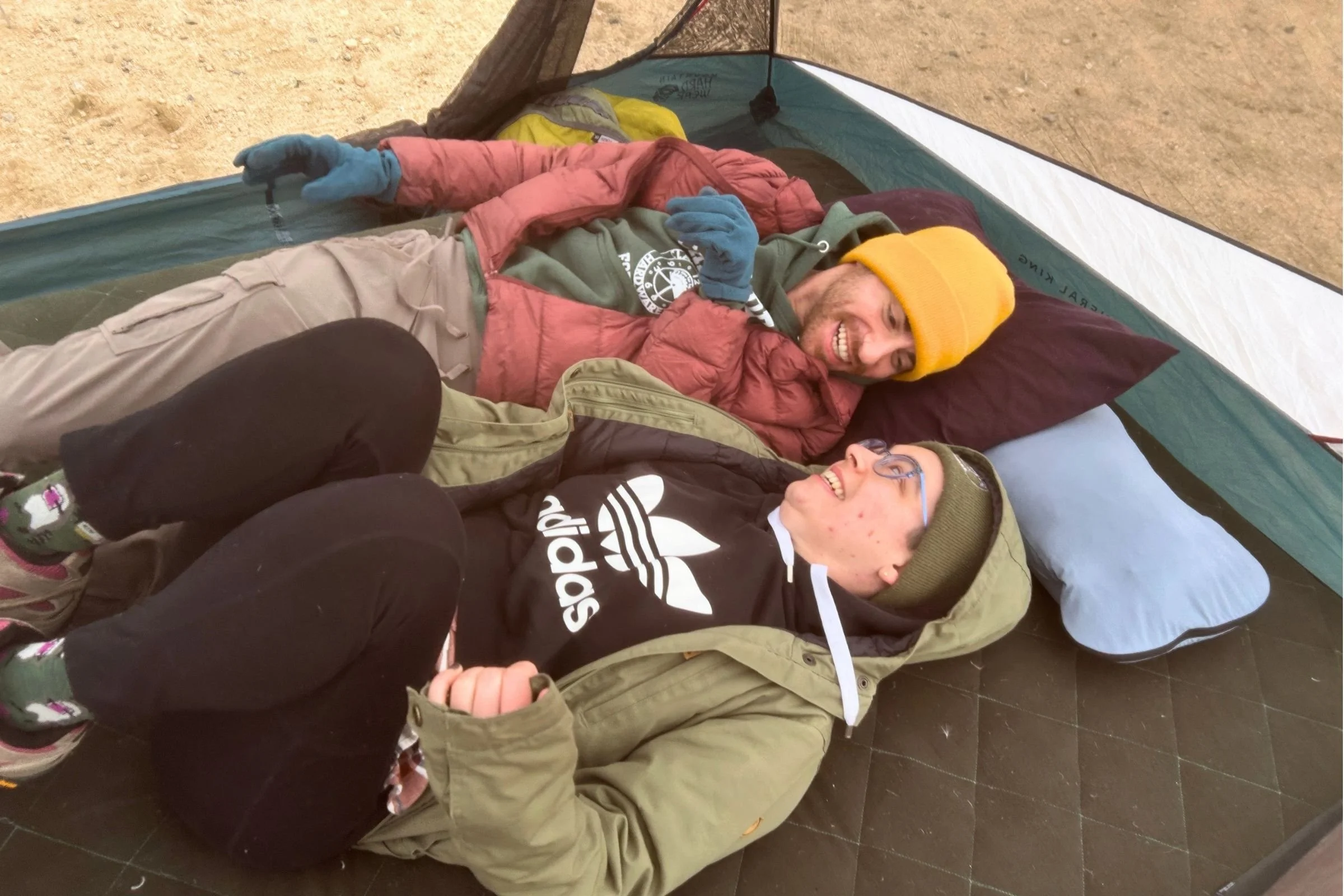   Two campers relax on the EXPED MegaMat Duo, highlighting its generous width and cushioned sleeping surface.  