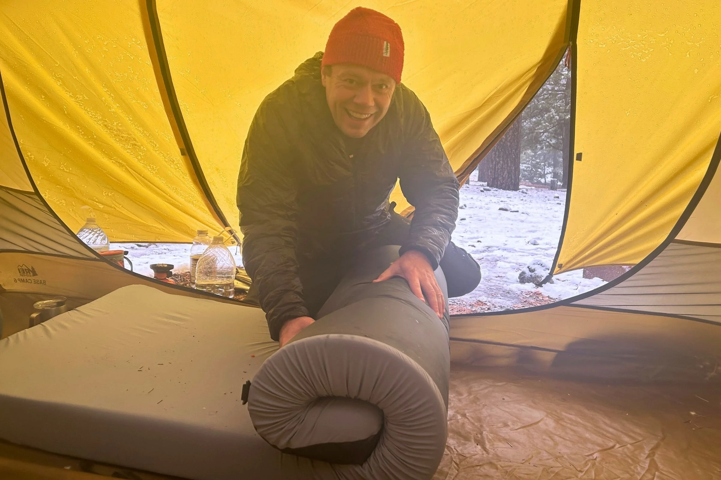   A tester sits on the HEST Sleep System Sleeping Pad inside a tent, showing its generous thickness and mattress-like cushioning.  