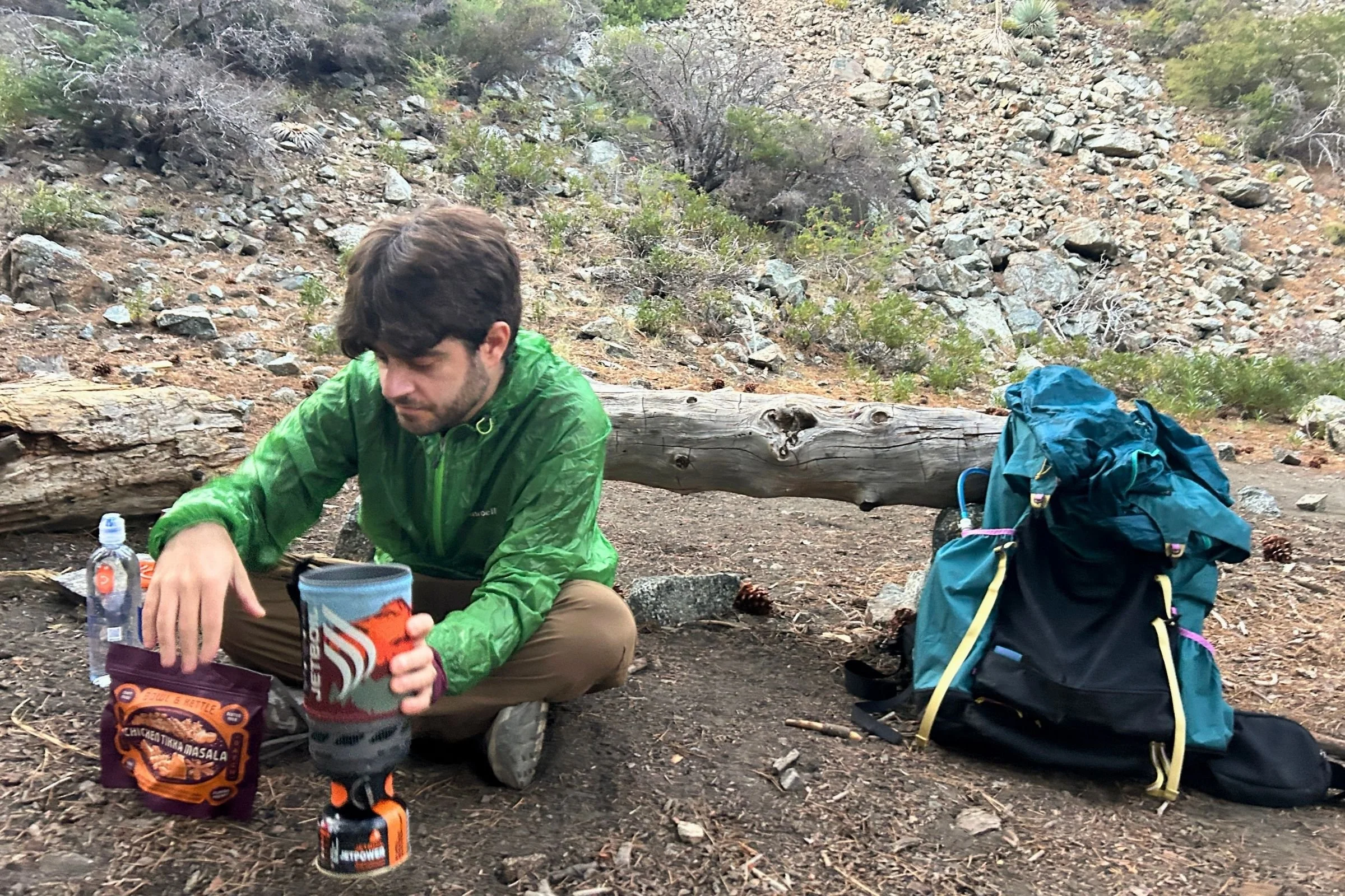   A backpacker accesses gear beside the Gossamer Gear Mariposa 60, with the pack’s large side pockets providing convenient storage for frequently used items.  