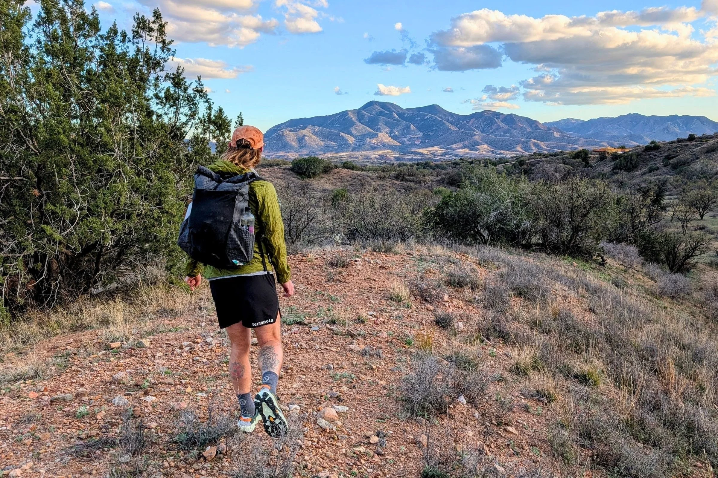   A backpacker hikes with the Pa’lante V2 with Joey Straps through open terrain, showing its compact profile and lightweight fastpacking design.  