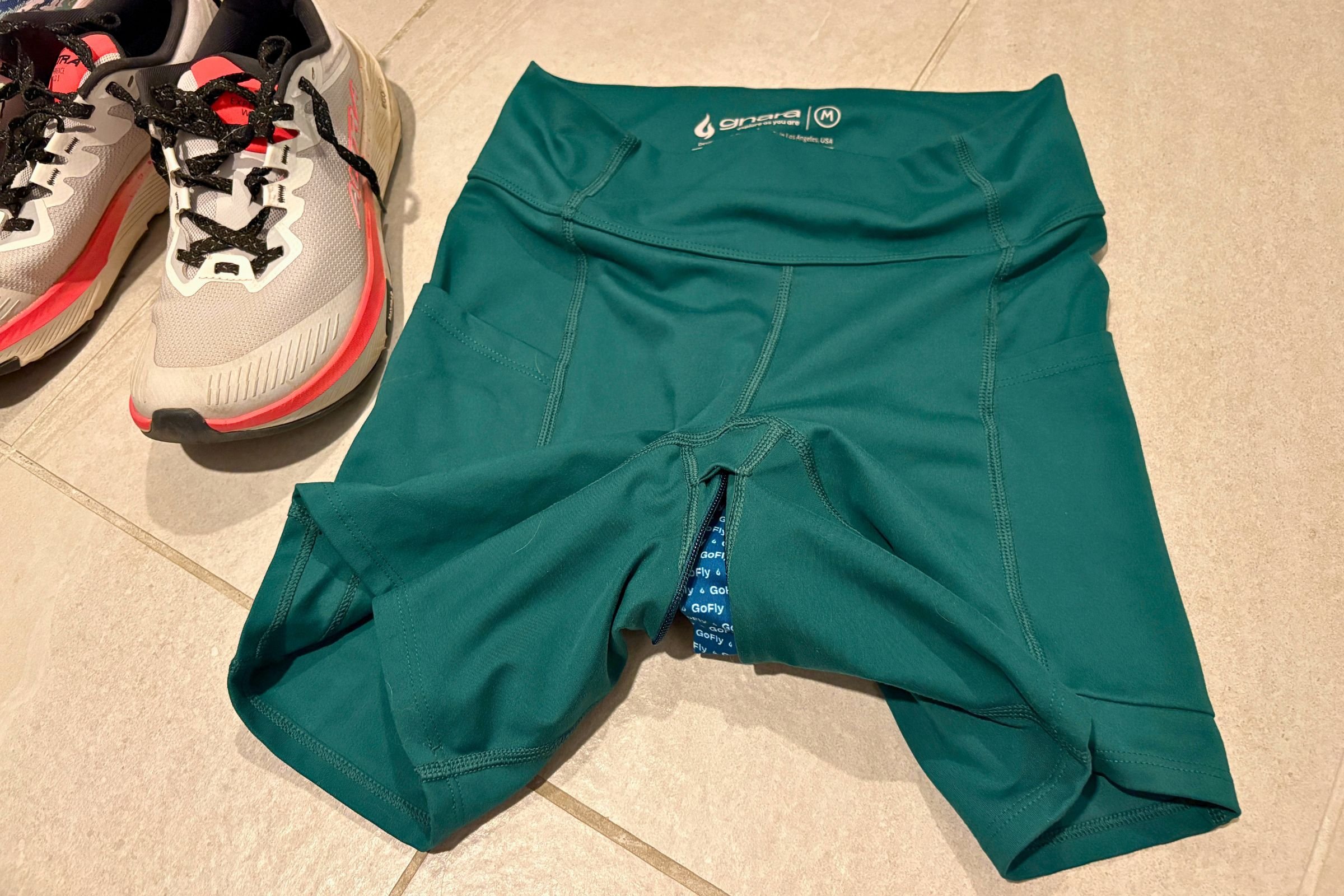   The Gnara Go Free shorts are laid flat beside running shoes, with the concealed GoFly zipper visible along the front and waistband.  