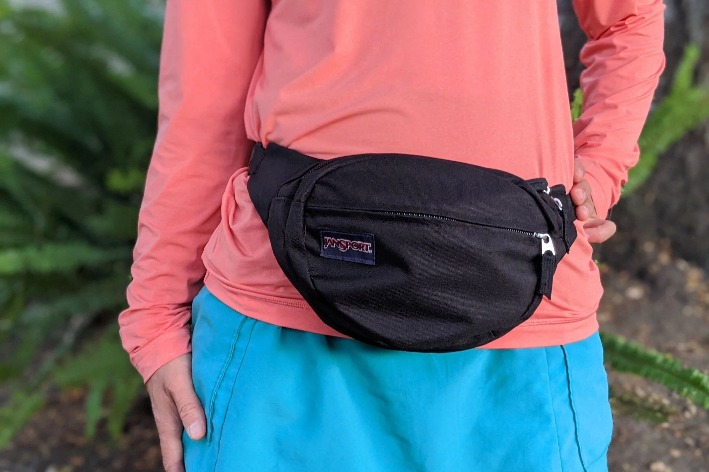   A hiker wears the JanSport Fifth Avenue Fanny Pack around the waist, showing its simple, classic design and compact 2.5-liter size.  