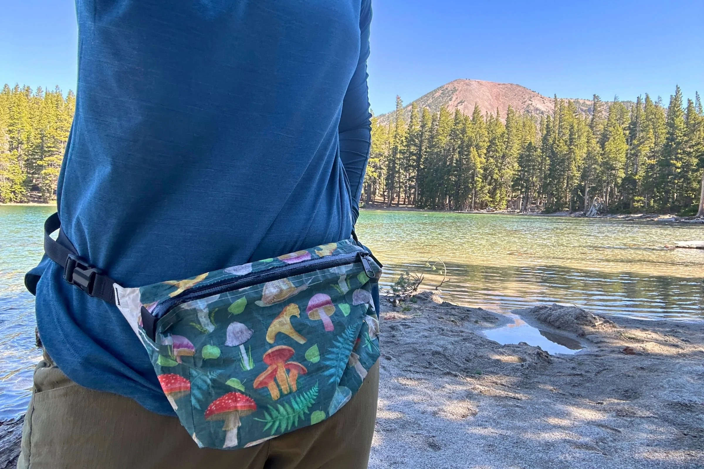   A hiker wears the High Tail Designs Ultralight Fanny Pack on the trail, showing its colorful design and compact 1-liter capacity.  
