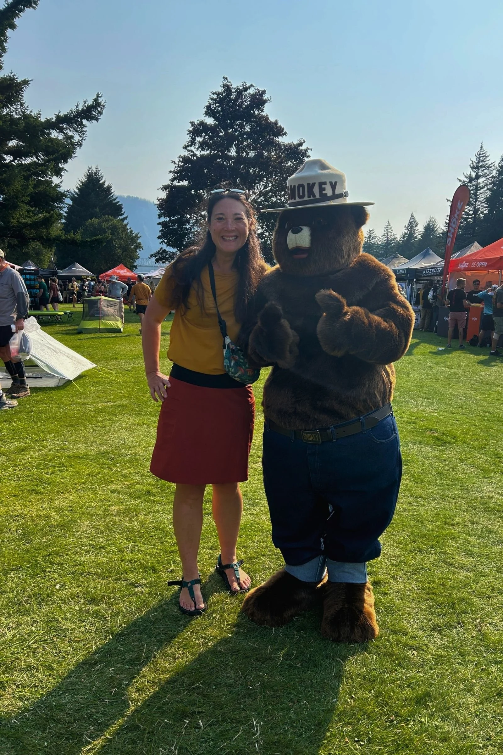   A hiker wearing the High Tail Designs Ultralight Fanny Pack poses with Smokey Bear, showing the colorful ultralight pack in use.  