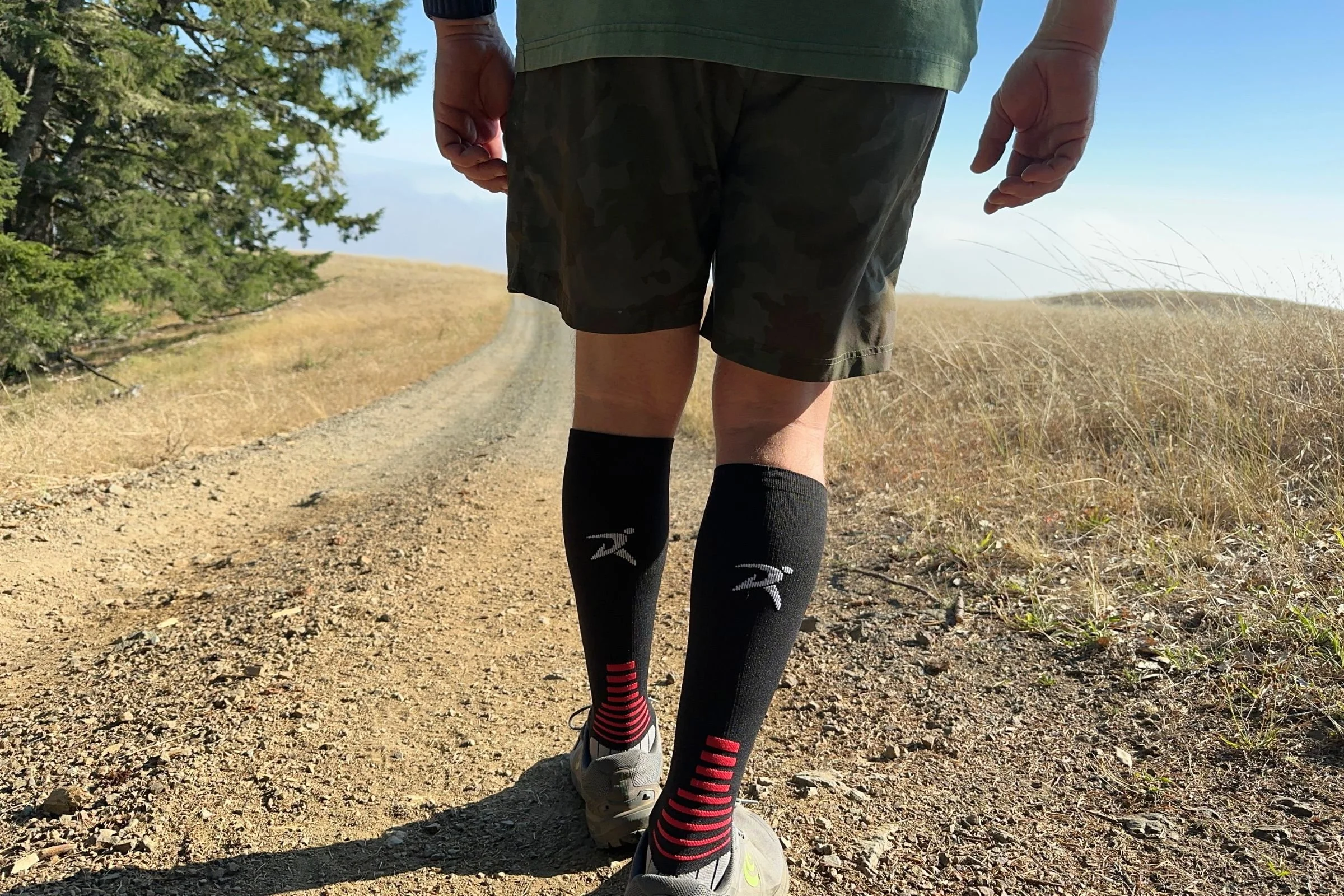   A runner wears the Rymora Compression Socks on a dirt trail, with the knee-high design providing graduated compression through the calves and cushioning underfoot for longer runs.  