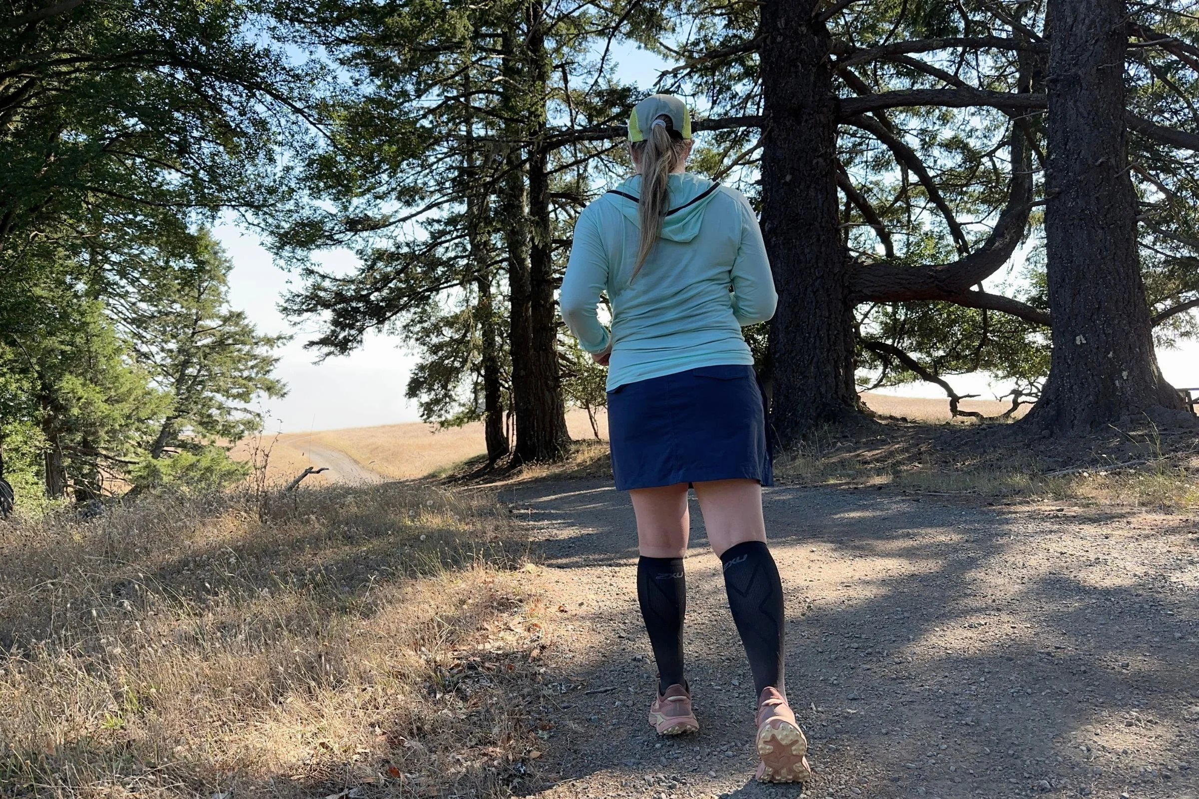   A runner wears the 2XU Vectr Cushion Full Length Compression Socks on a wooded trail, where their graduated compression and X-LOCK foot support provide a secure, supportive fit over longer distances.  