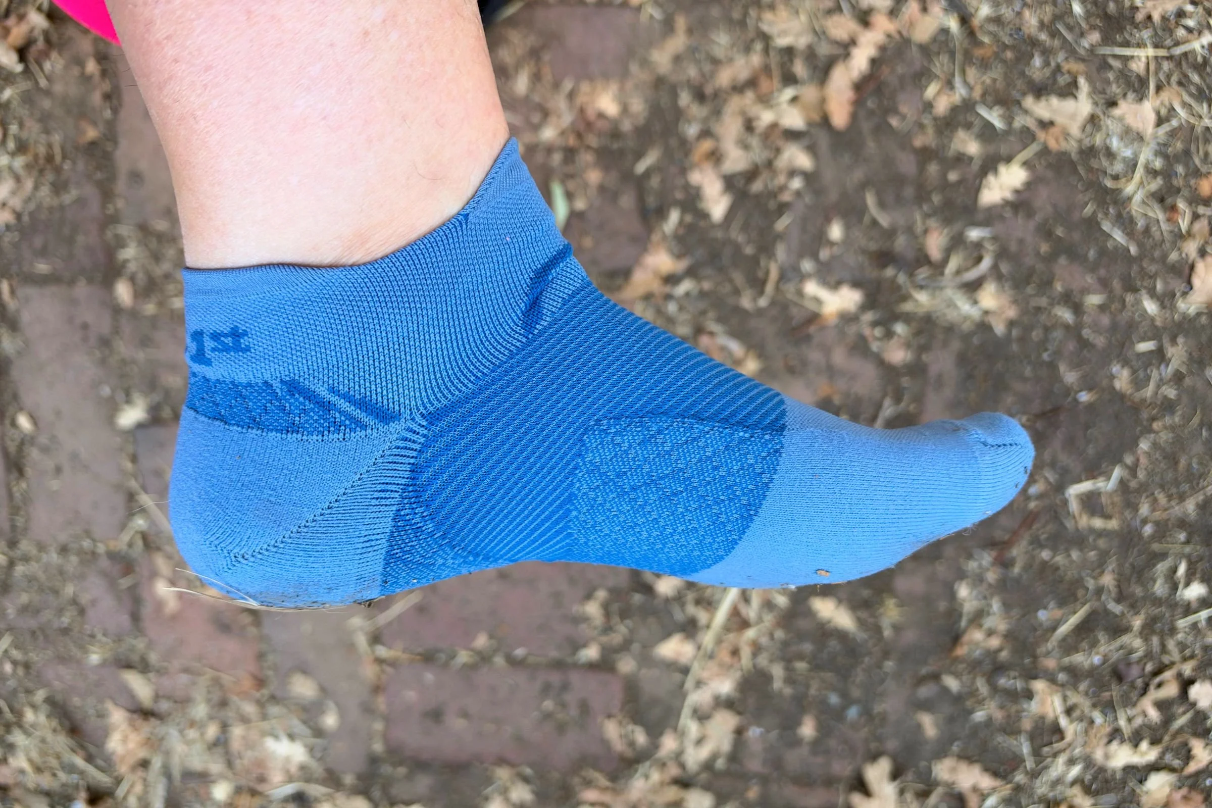   A side view of the blue OS1st Plantar Fasciitis Quarter Crew Sock reveals its snug ankle fit and targeted compression around the arch and heel, designed to provide extra foot support during runs.  