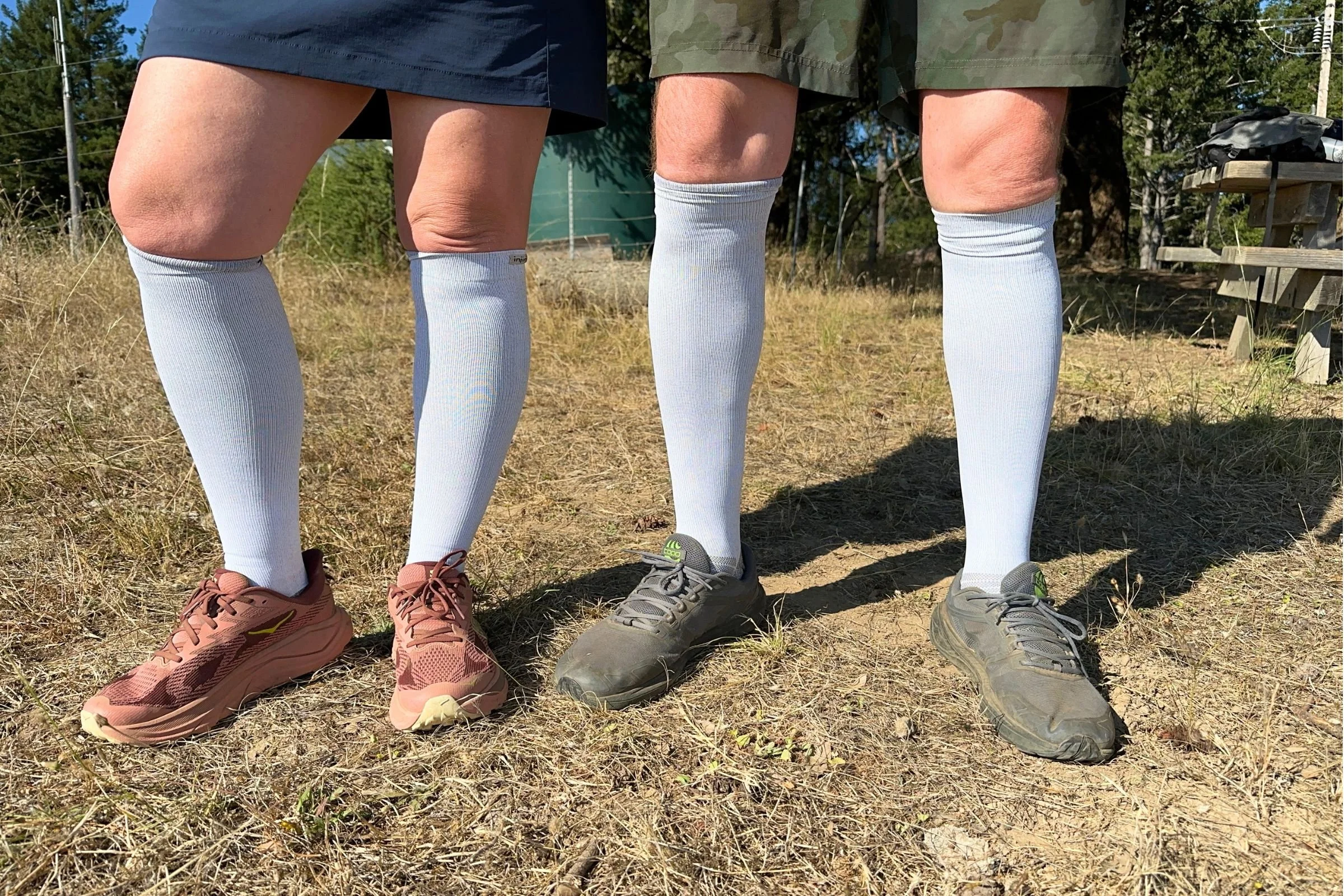   Two testers wear the Injinji Compression Over the Calf Socks in white during outdoor testing. These lightweight compression socks feature individual toe pockets designed to help reduce friction and blisters while running.  