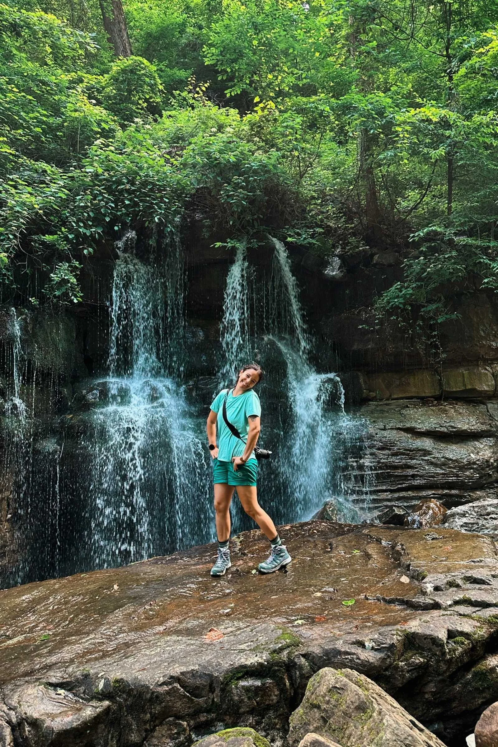 A hiker posing for a picture in front of a waterfall, wearing the Suunto Race 2