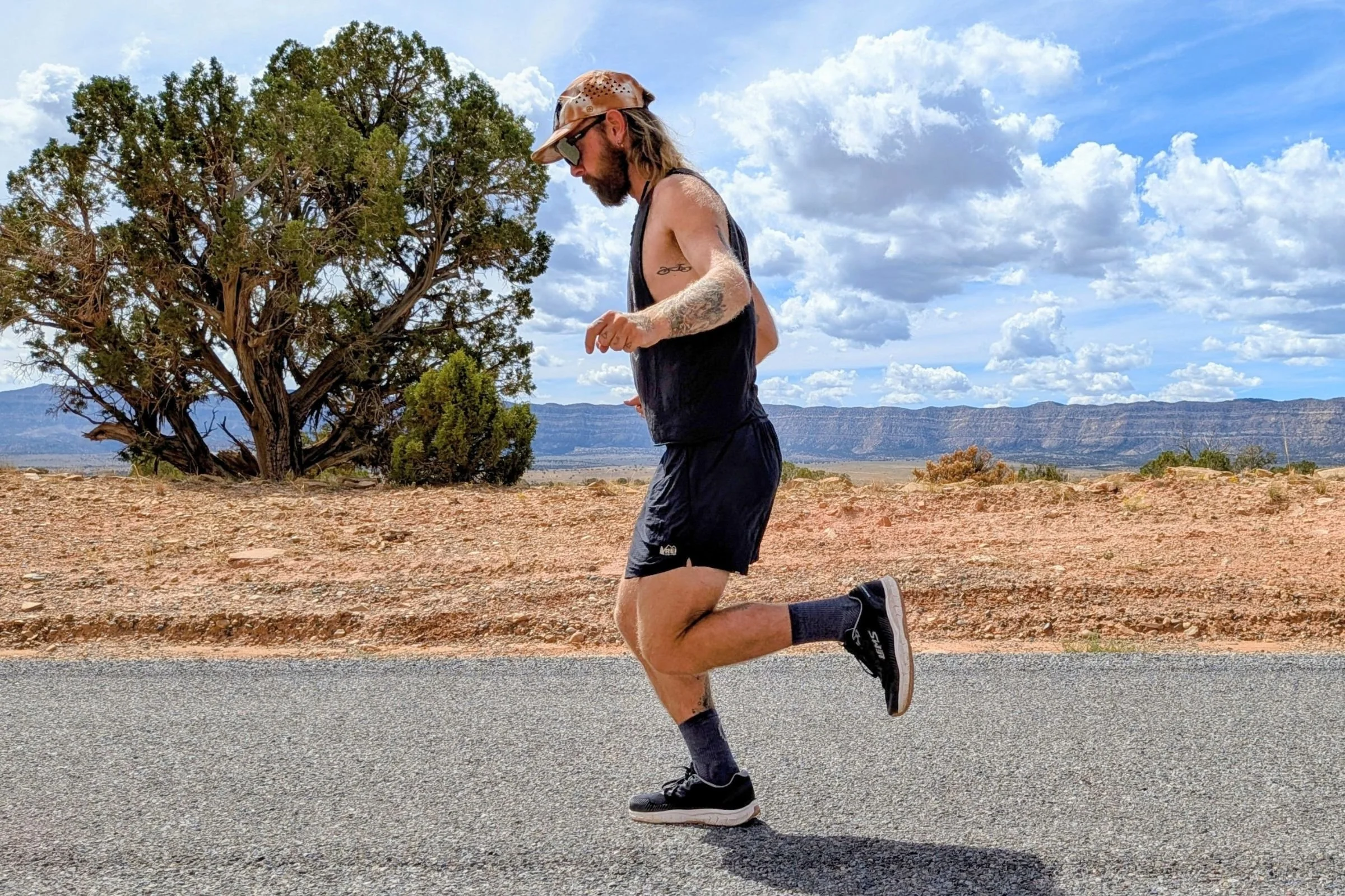 Man in a black tank top and shorts wearing black Lems ZENSPEED+ running shoes while running on a road.