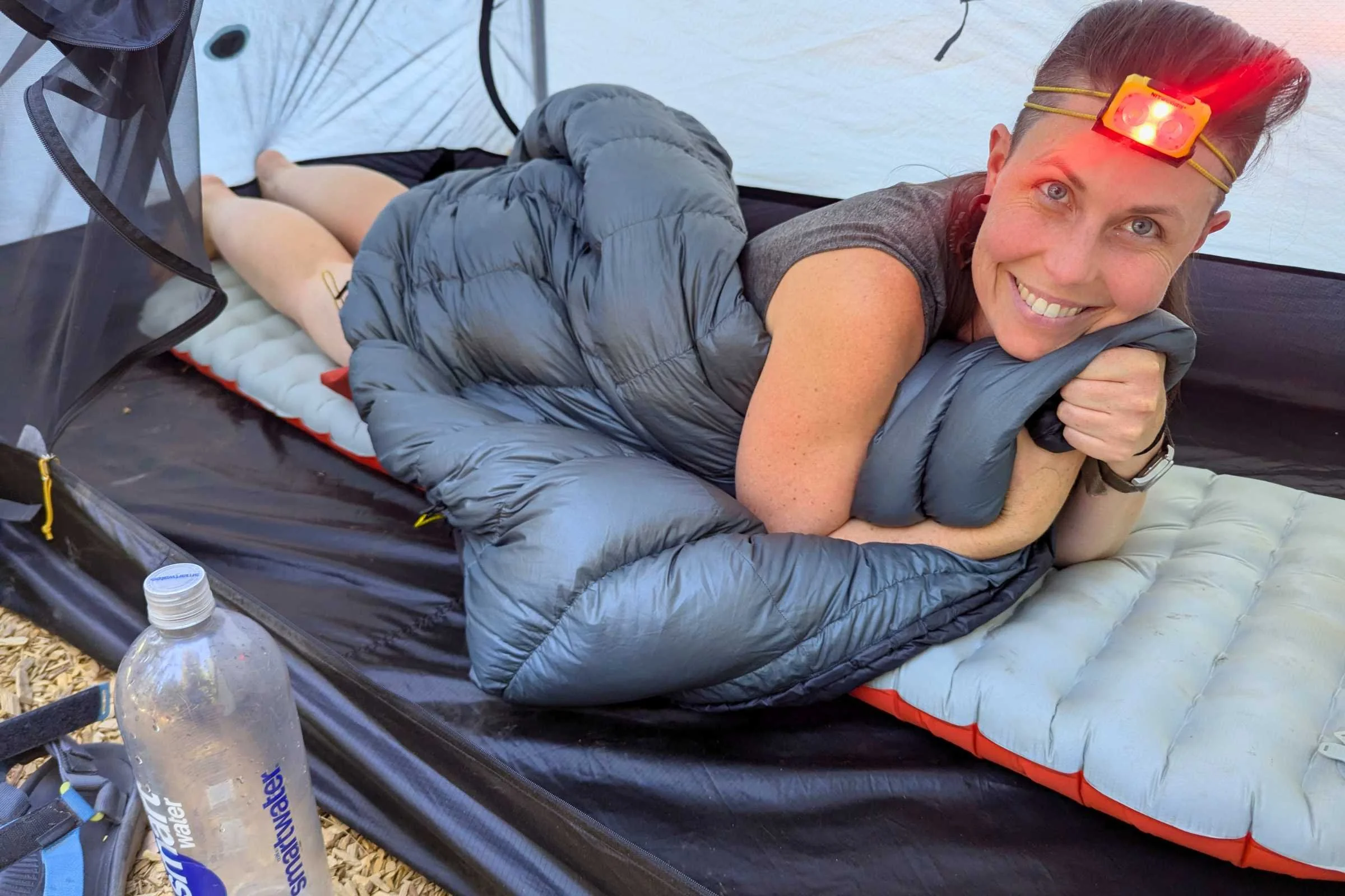 Woman relaxing inside a tent while wearing the Nitecore NU25 MCT headlamp in red-light mode.