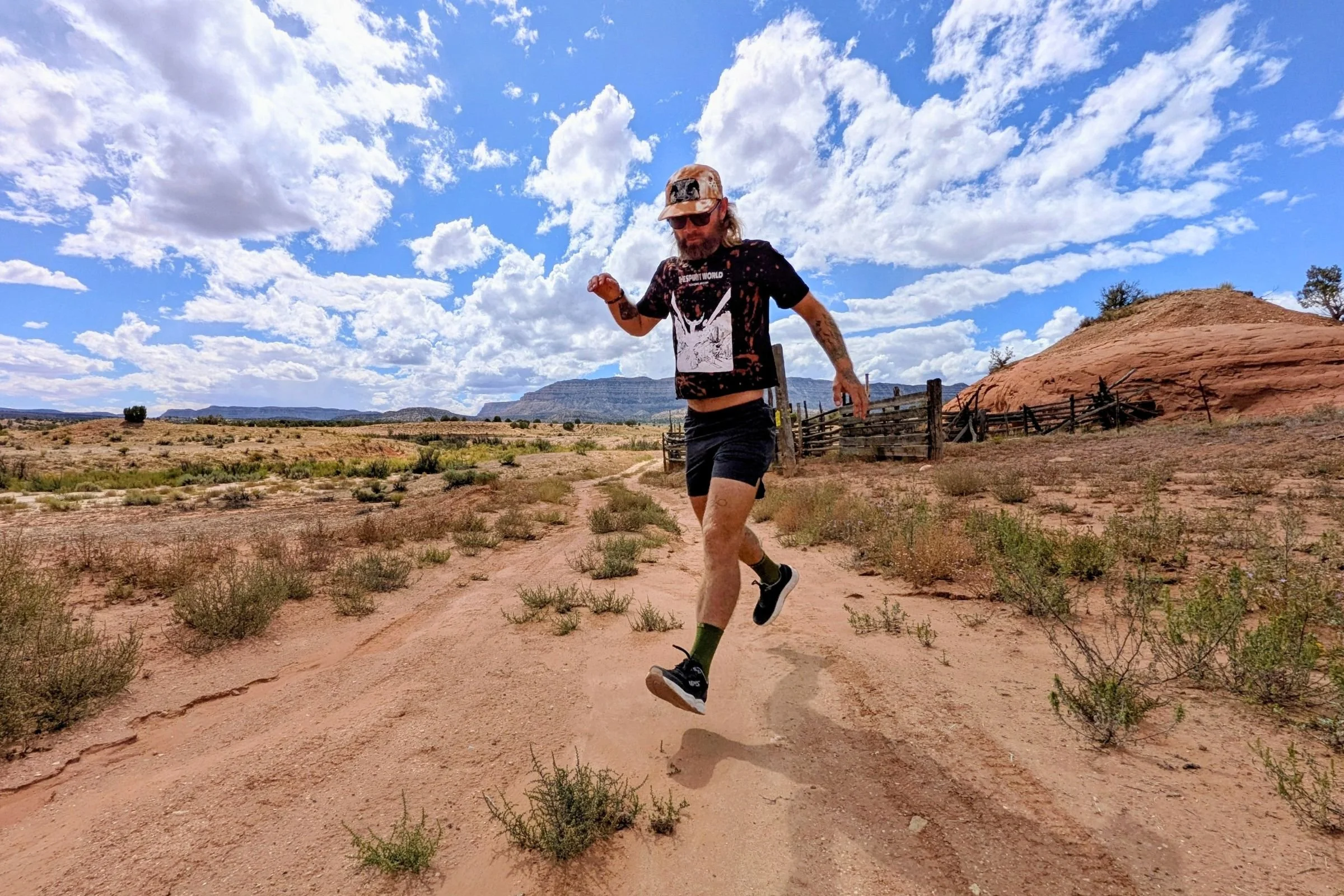Man wearing Lems ZENSPEED+ shoes and running along a dirt road in a desert landscape.