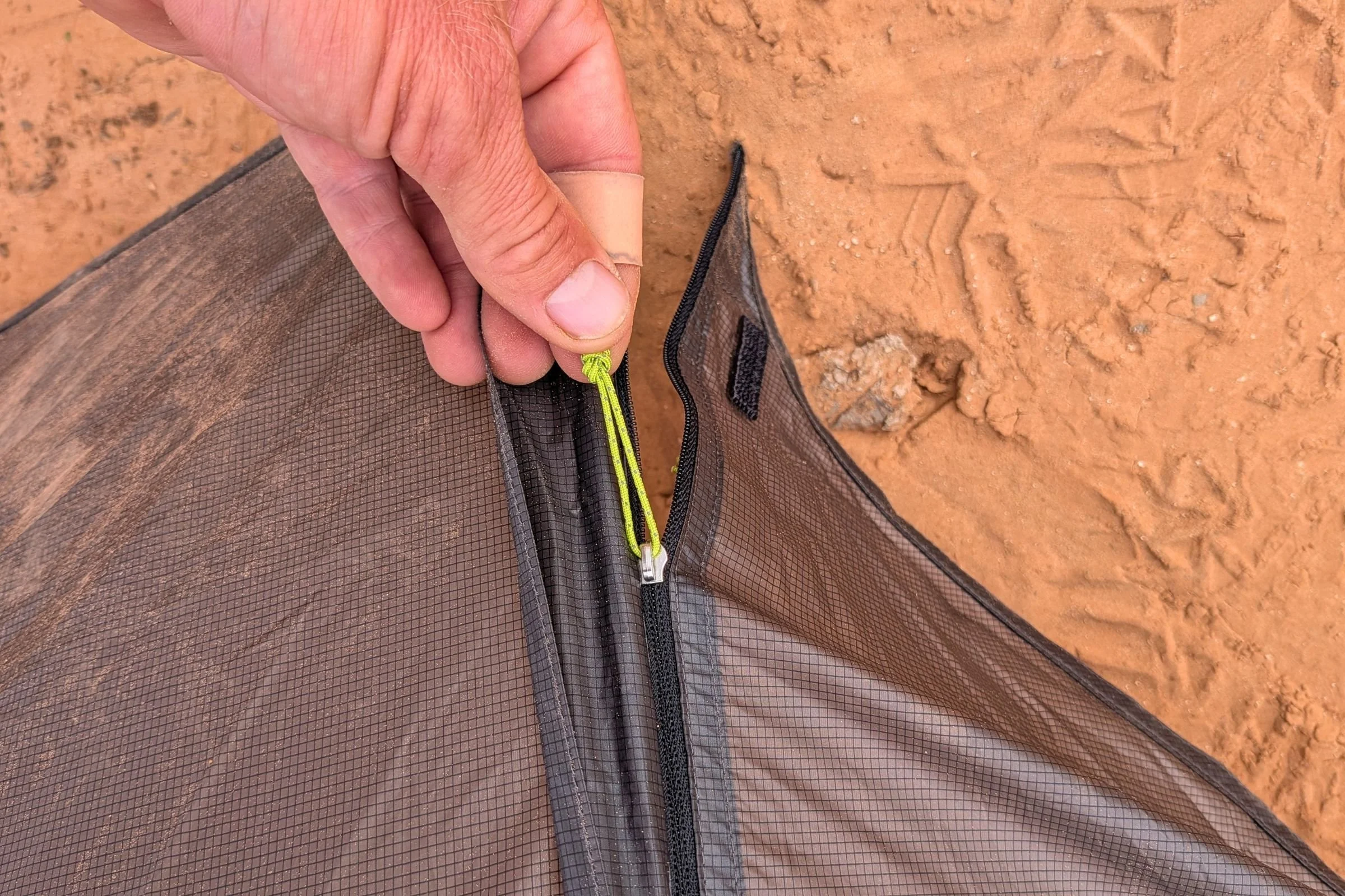 A hand holds the zipper pull on the mesh door of Gossamer Gear The Free.