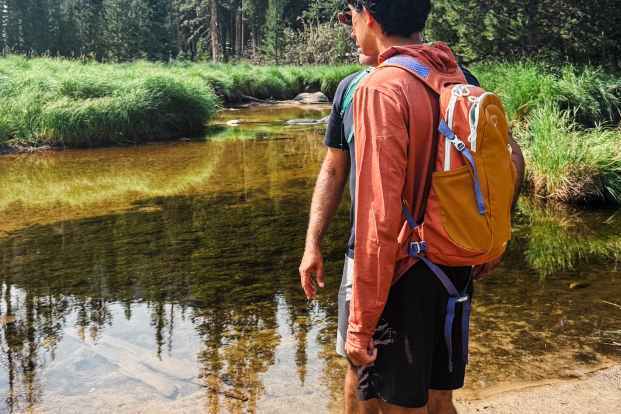 A person wearing the Osprey Daylite backpack on a hike with a mountain pond in the background.