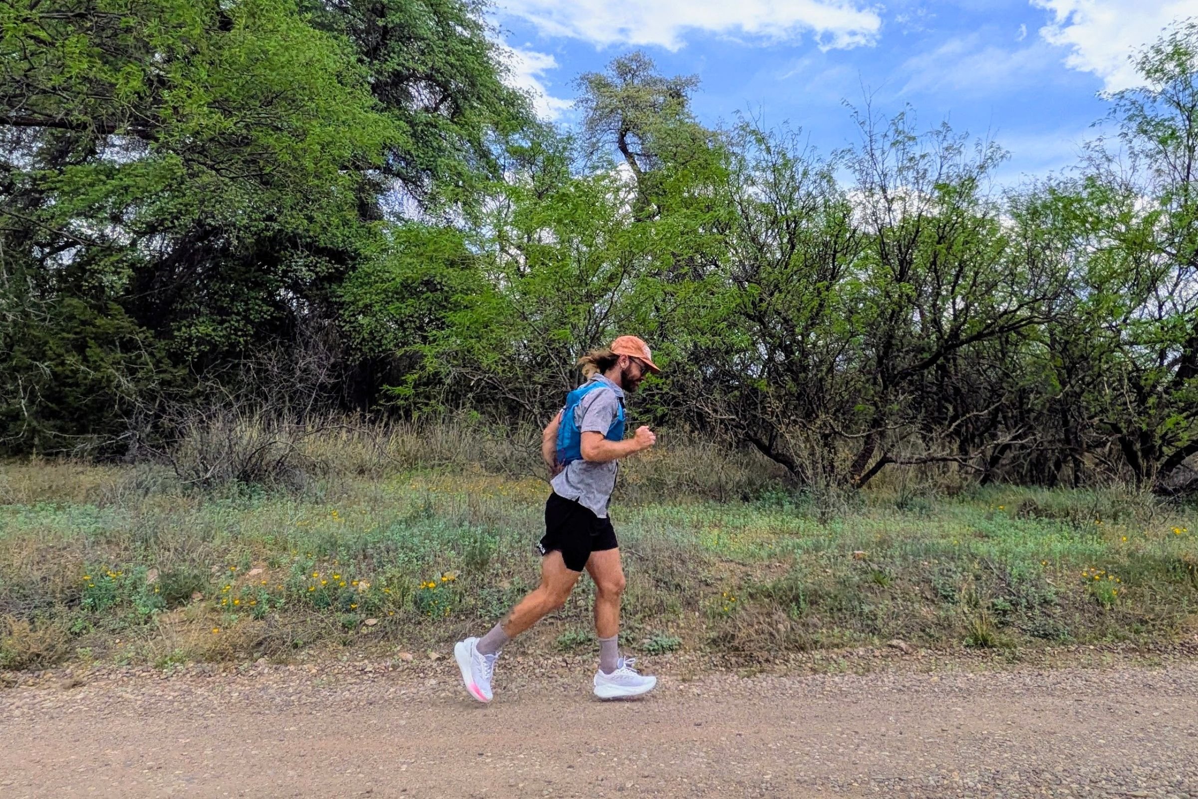 Man running along a tree-lined dirt road while wearing a Nathan VaporAir pack.
