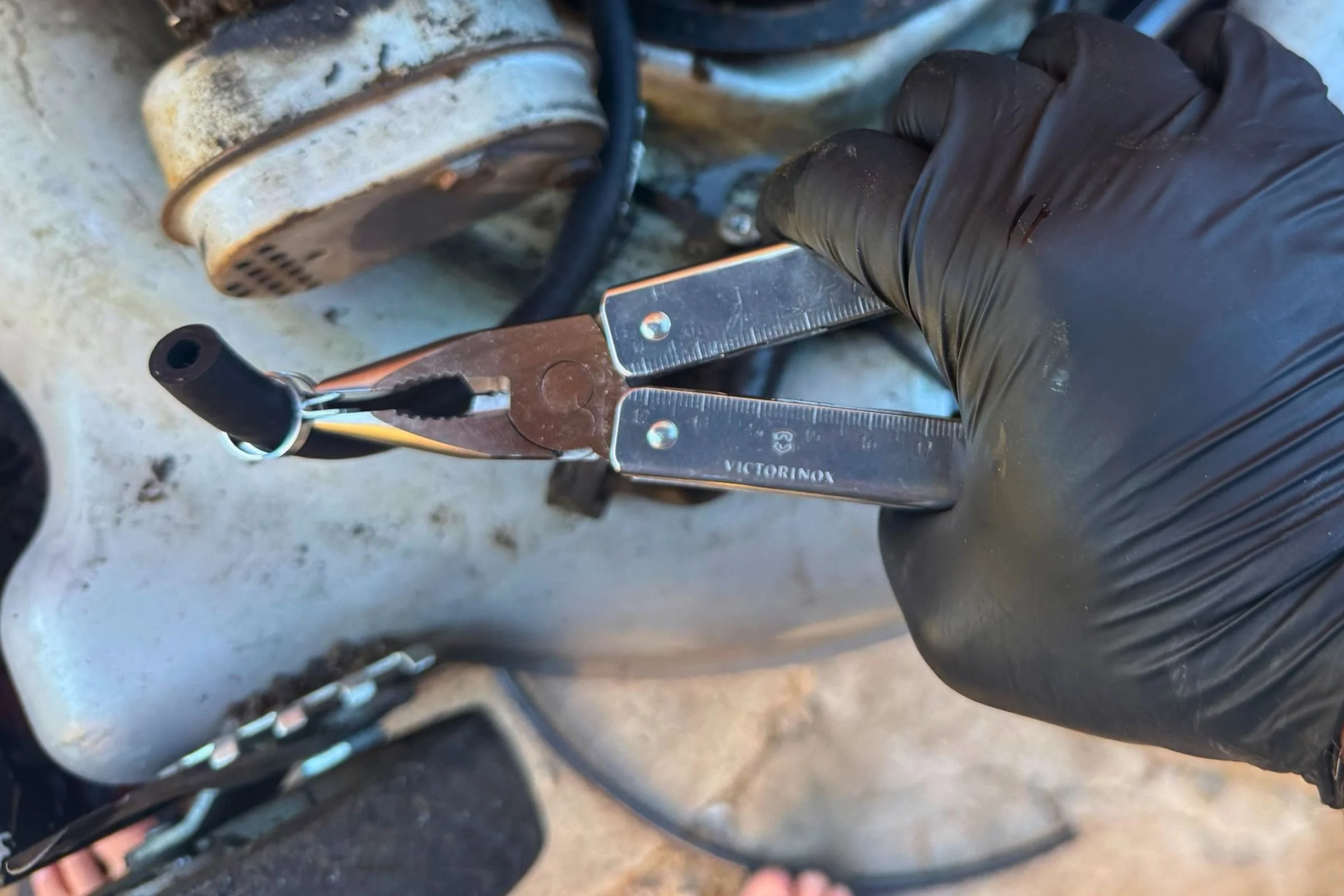 Victorinox Swiss Tool X needle-nose pliers gripping a spring clamp on a fuel hose.