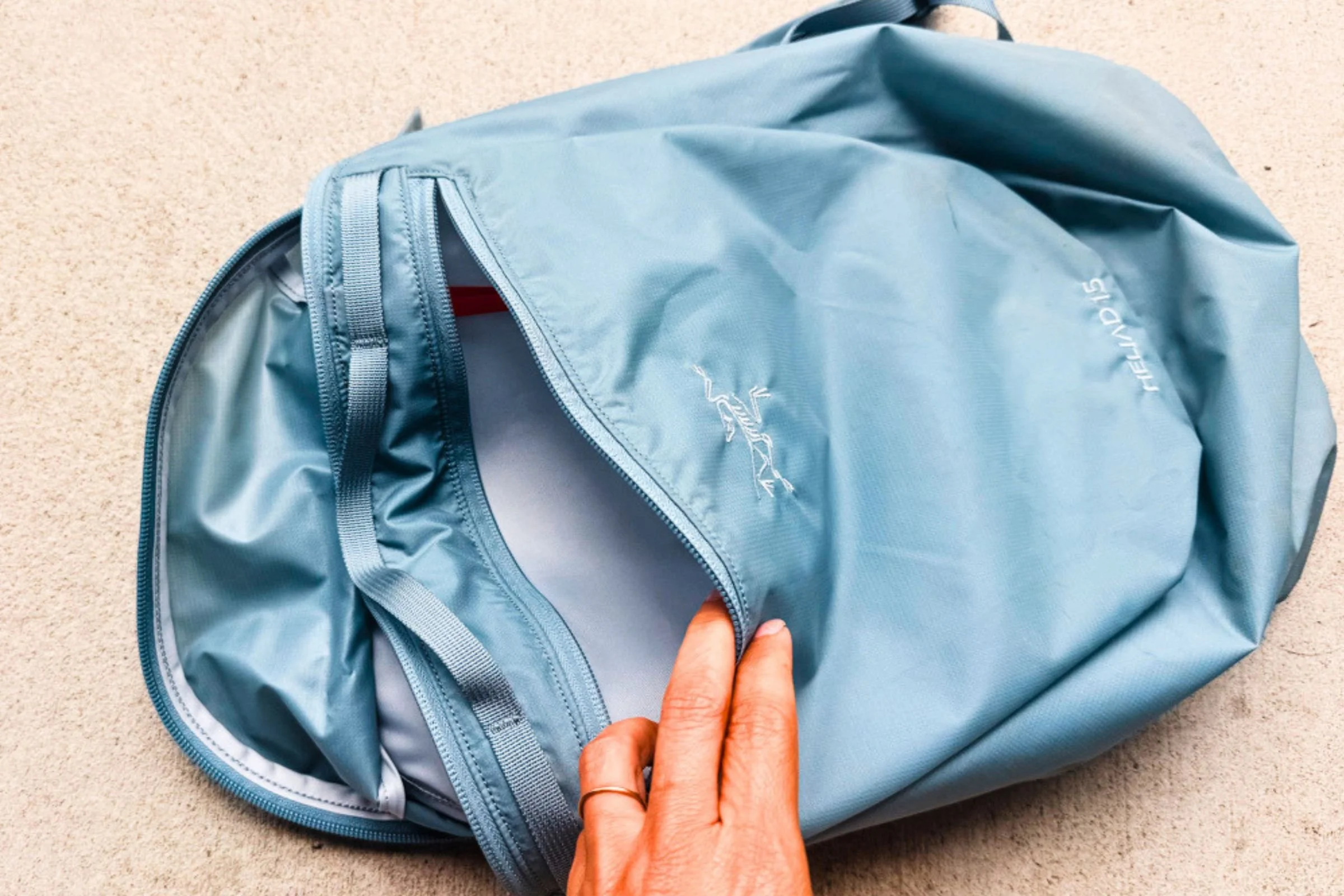 A hand opening the front zippered pocket of an Arc’teryx Heliad 15 backpack.