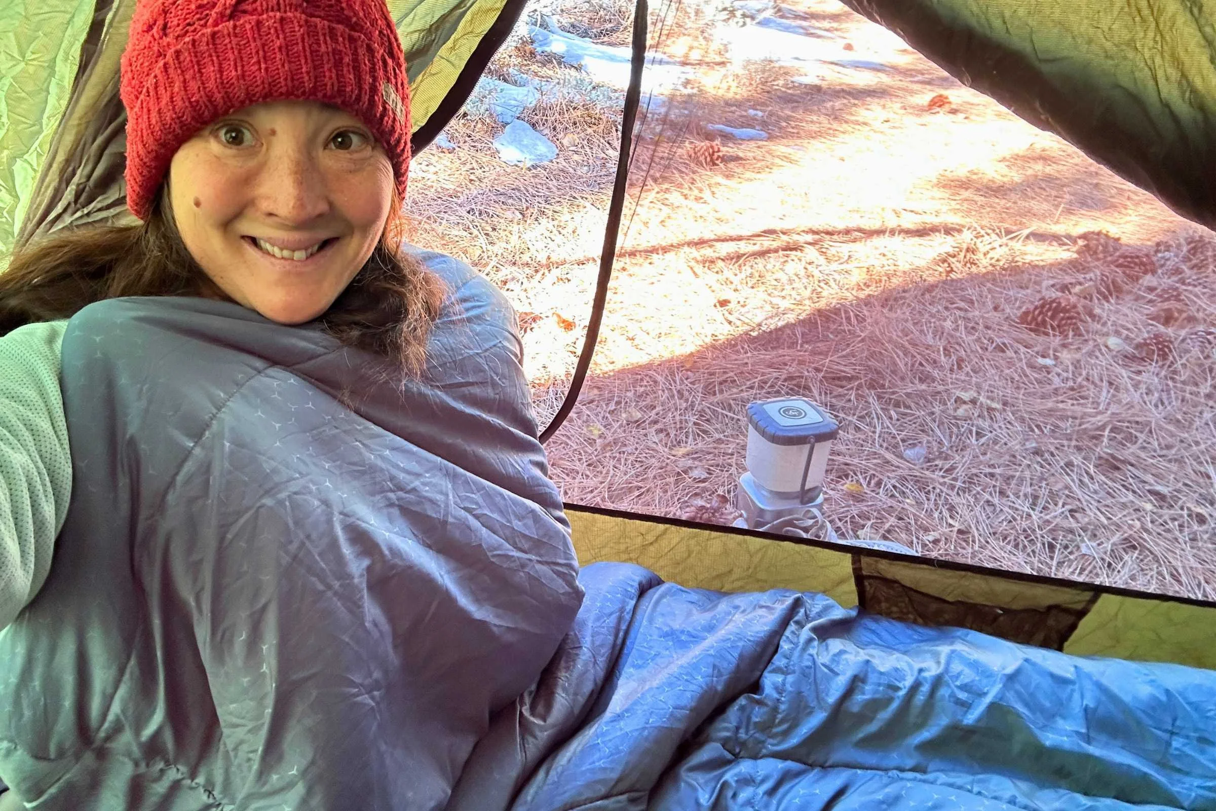 the author wearing a red hat and sitting in the exped deepsleep in her tent