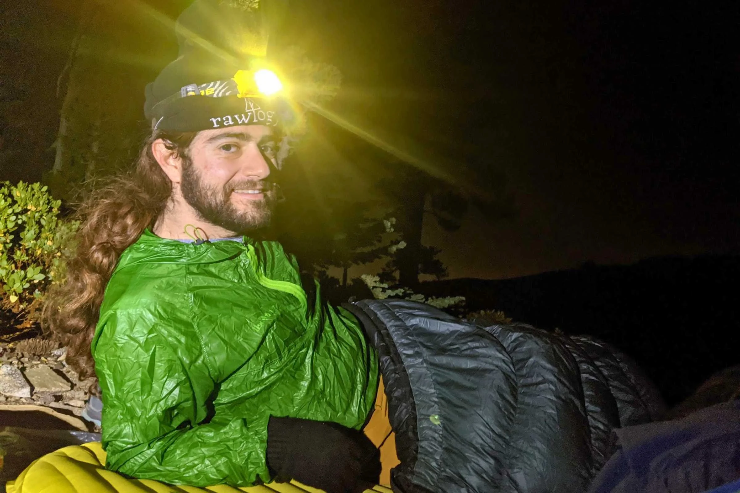 Man in sleeping bag wearing a Nitecore NU25 Classic (discontinued, but similar to the NU20) headlamp